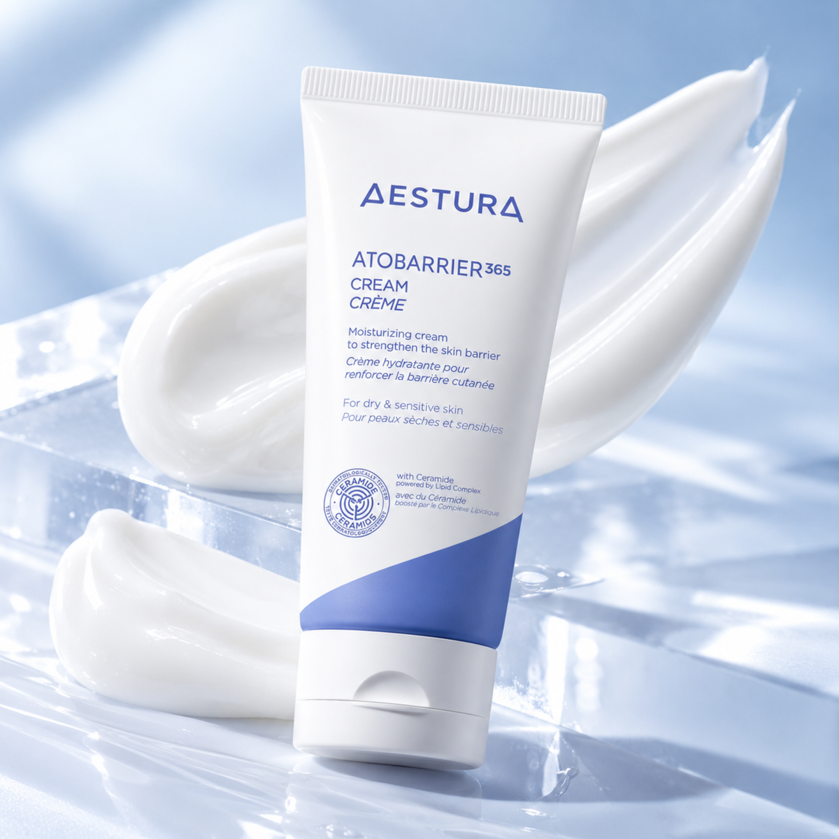 A squeeze tube of Aestura Atobarrier365 Cream Crème standing upright on a glossy, icy blue surface, with dollops of white cream arranged behind it.