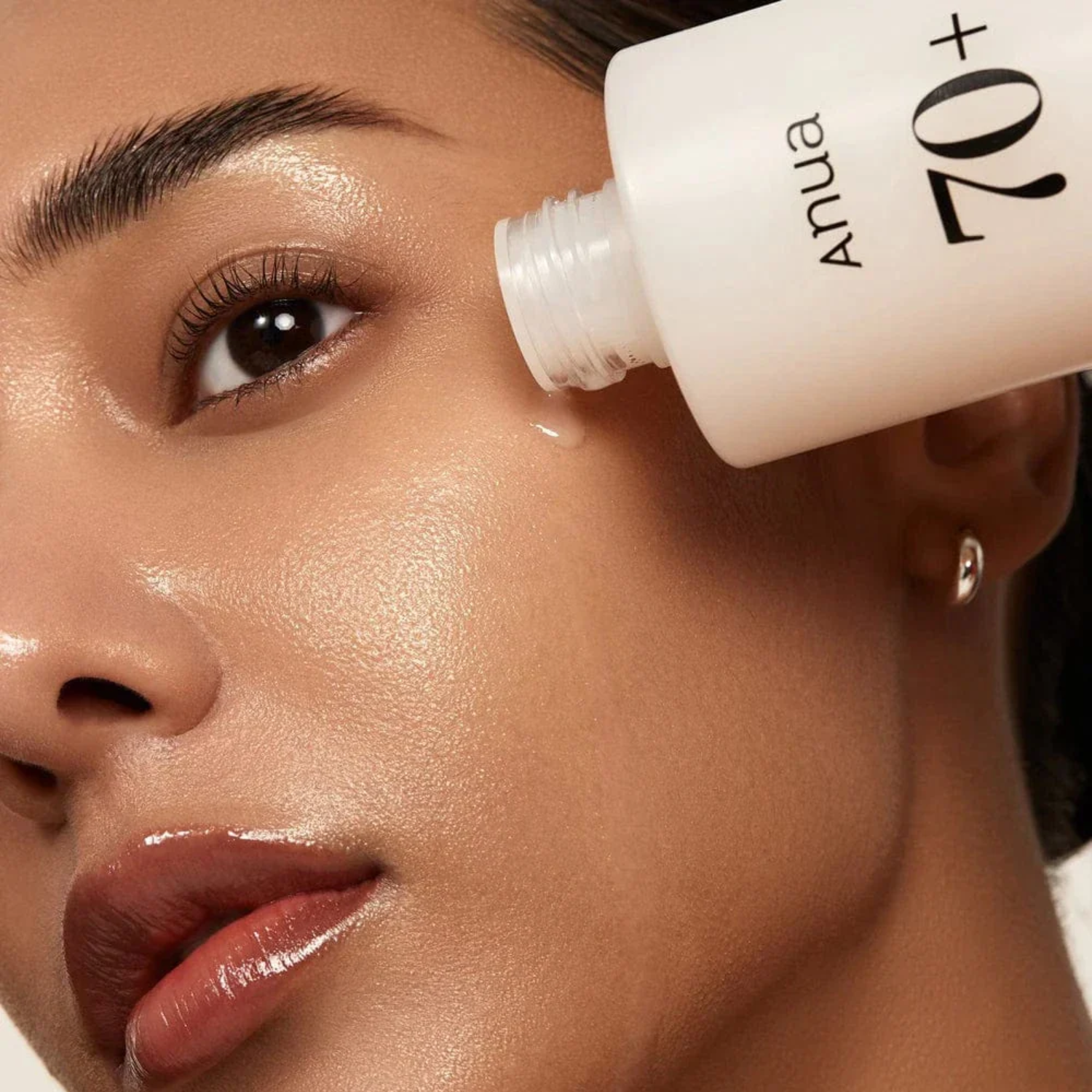 Woman applying a skincare product labeled 'Anua' to her face.