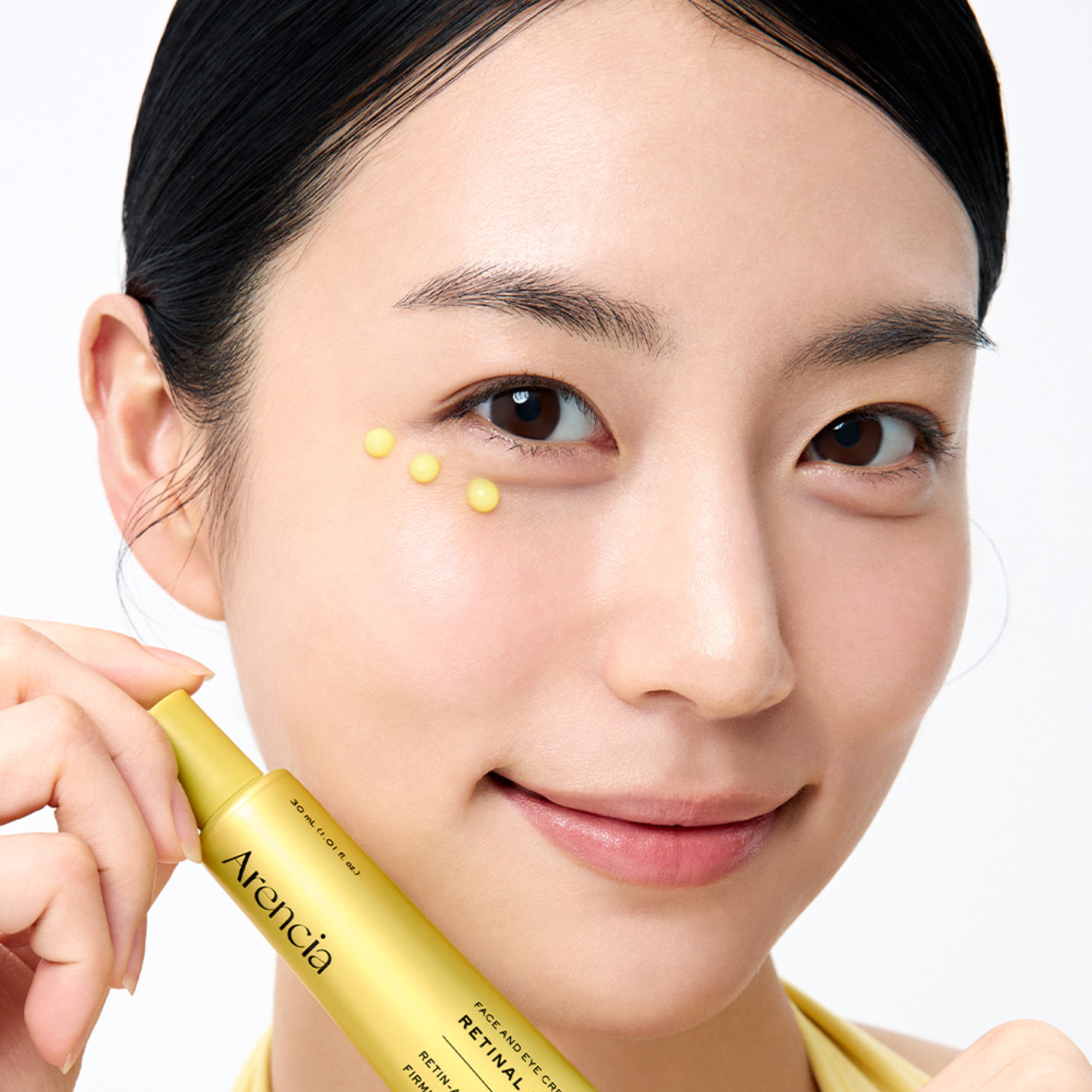 Woman applying a yellow cosmetic product to her face with a focus on the brand 'Arencia'.