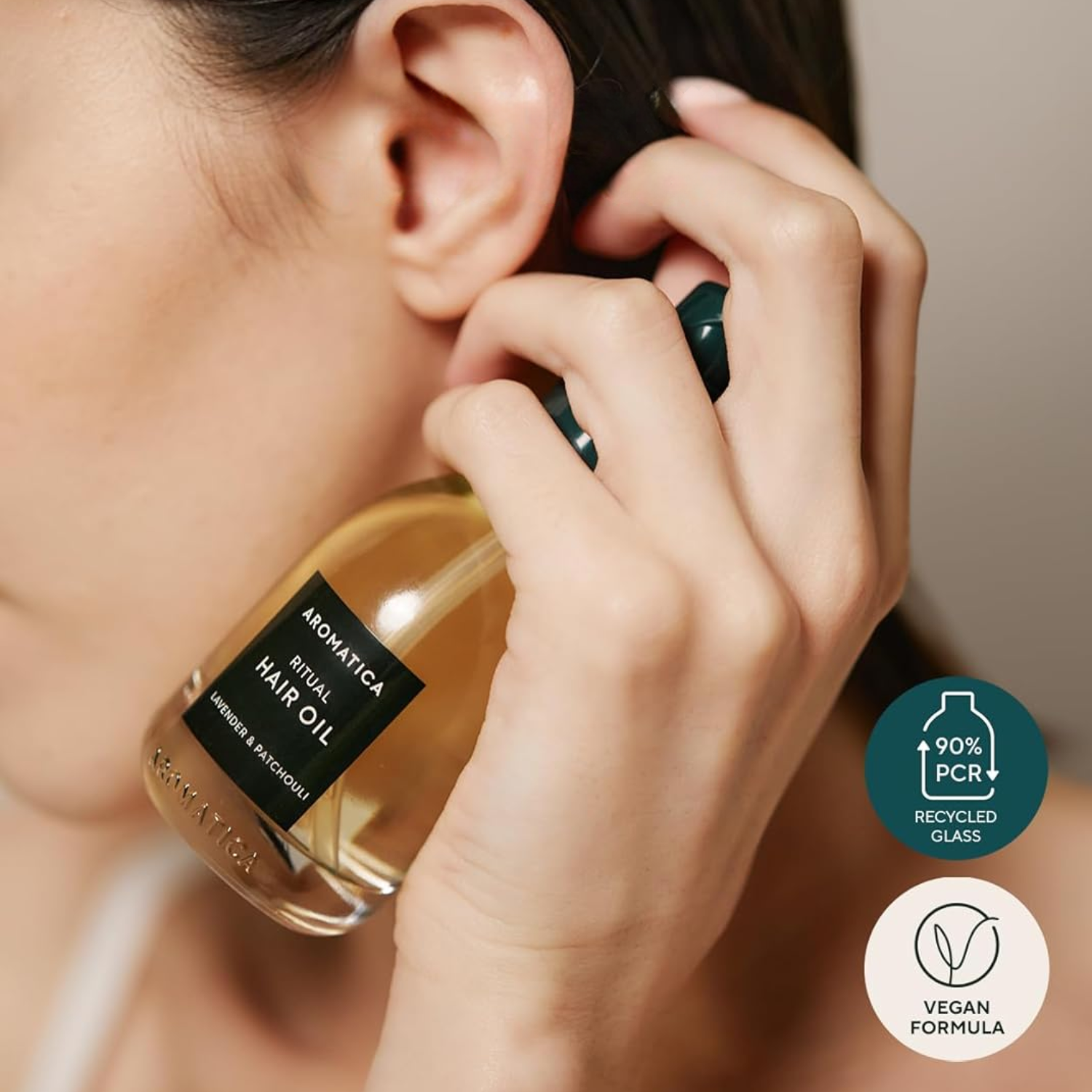 Person holding a bottle of hair oil with 'Bramatica Ritual' branding, featuring recycled glass and vegan formula icons.