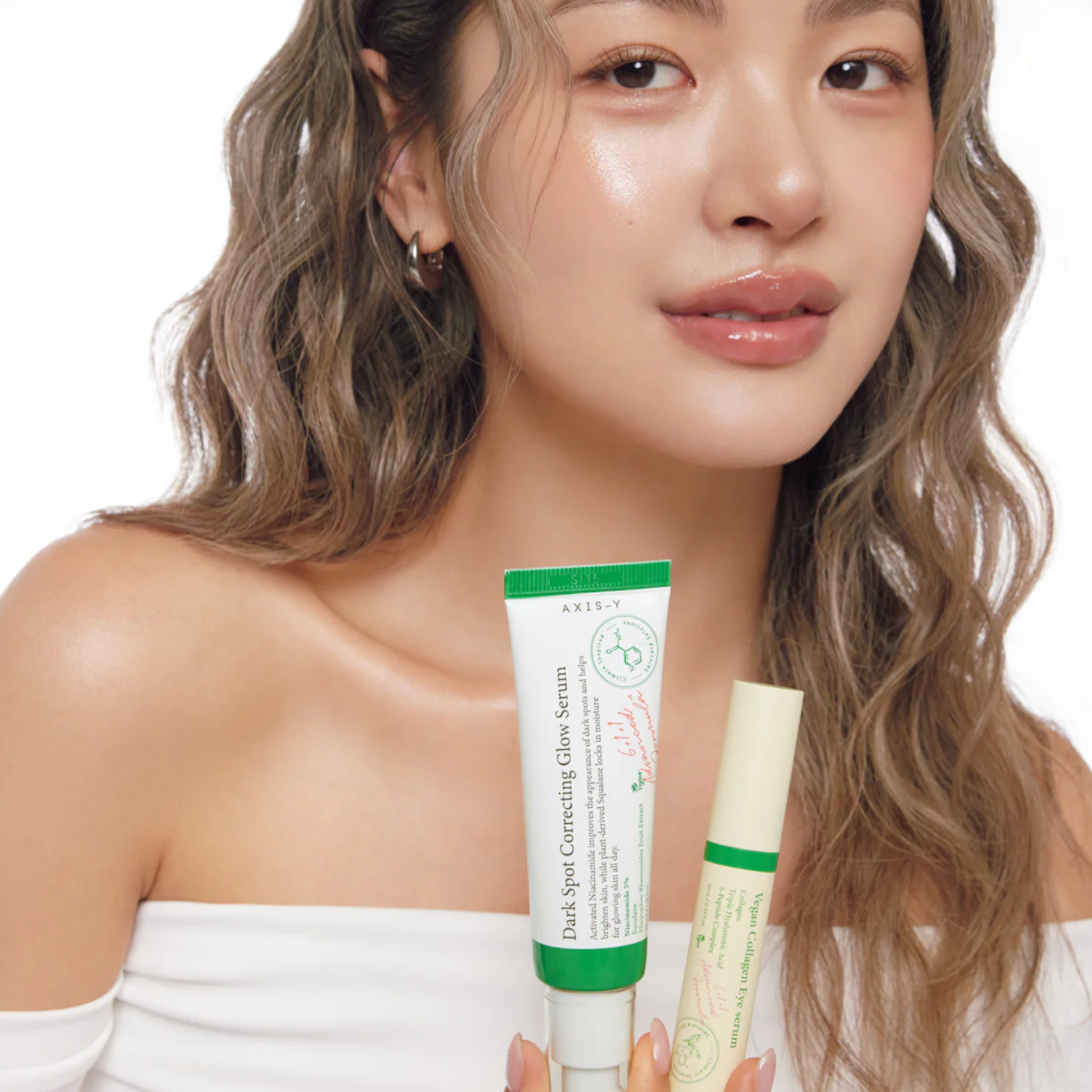 Woman holding two skincare products against a white background