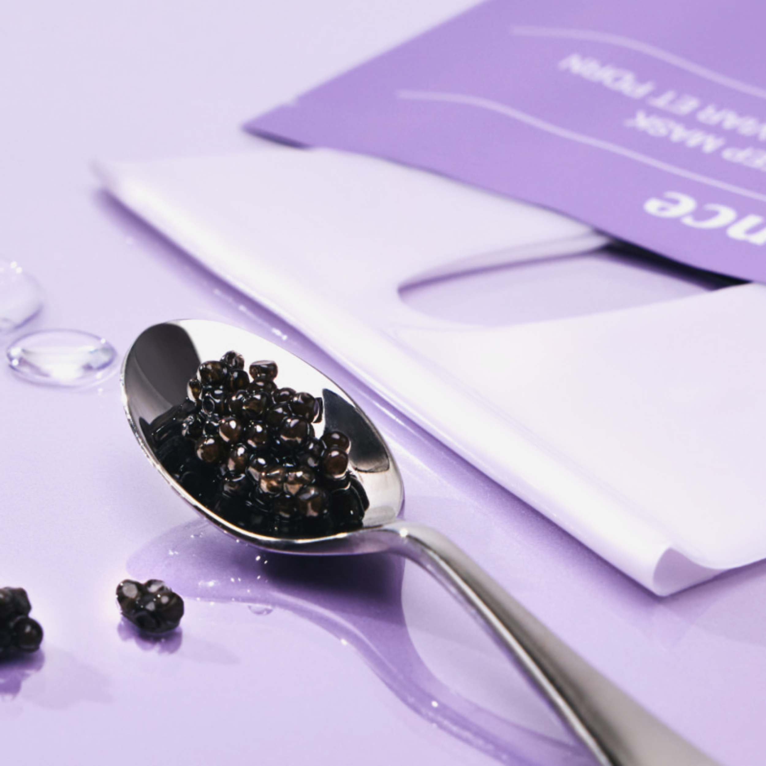 Spoon with black caviar on a purple surface with a white napkin and card.