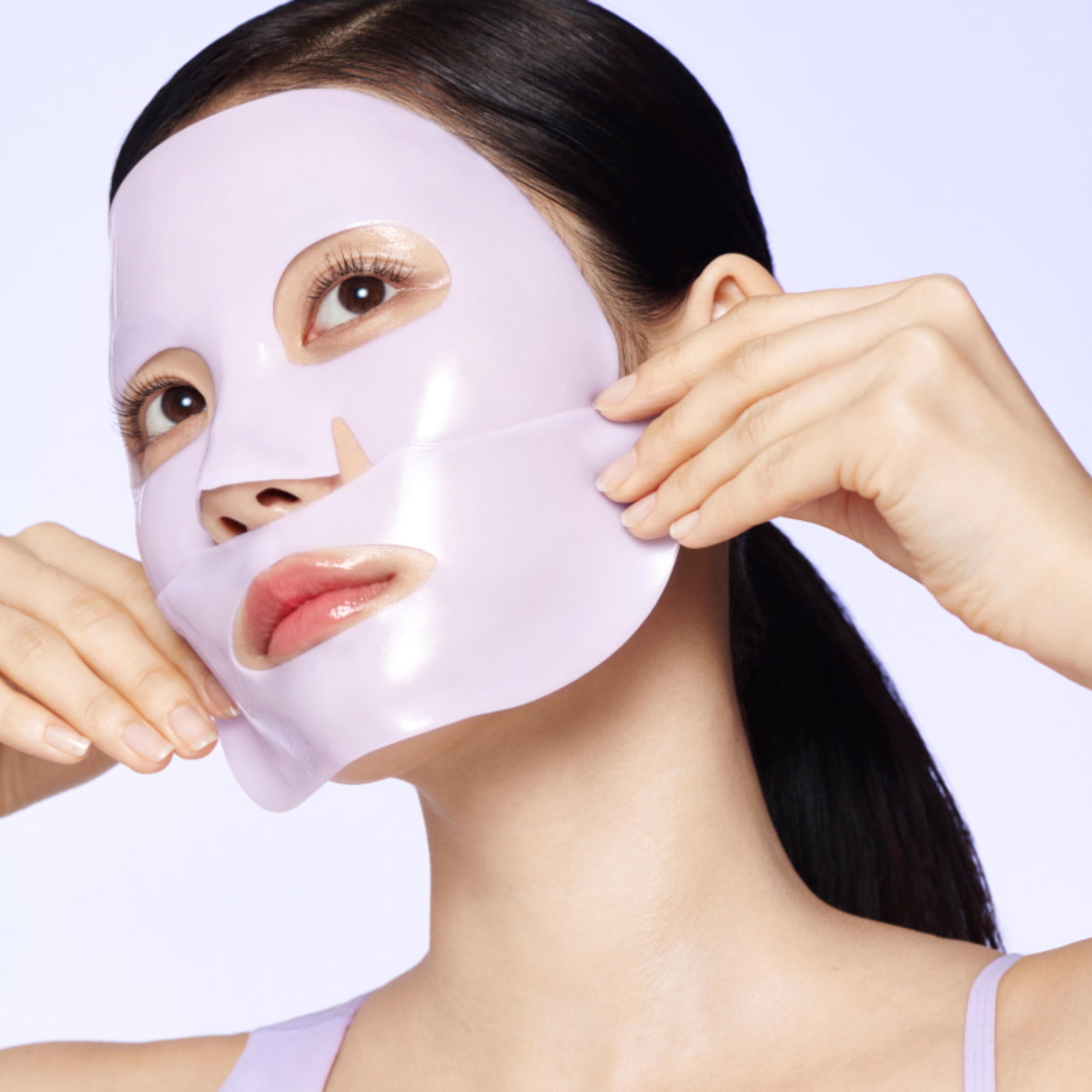 Woman applying a white face mask against a light purple background
