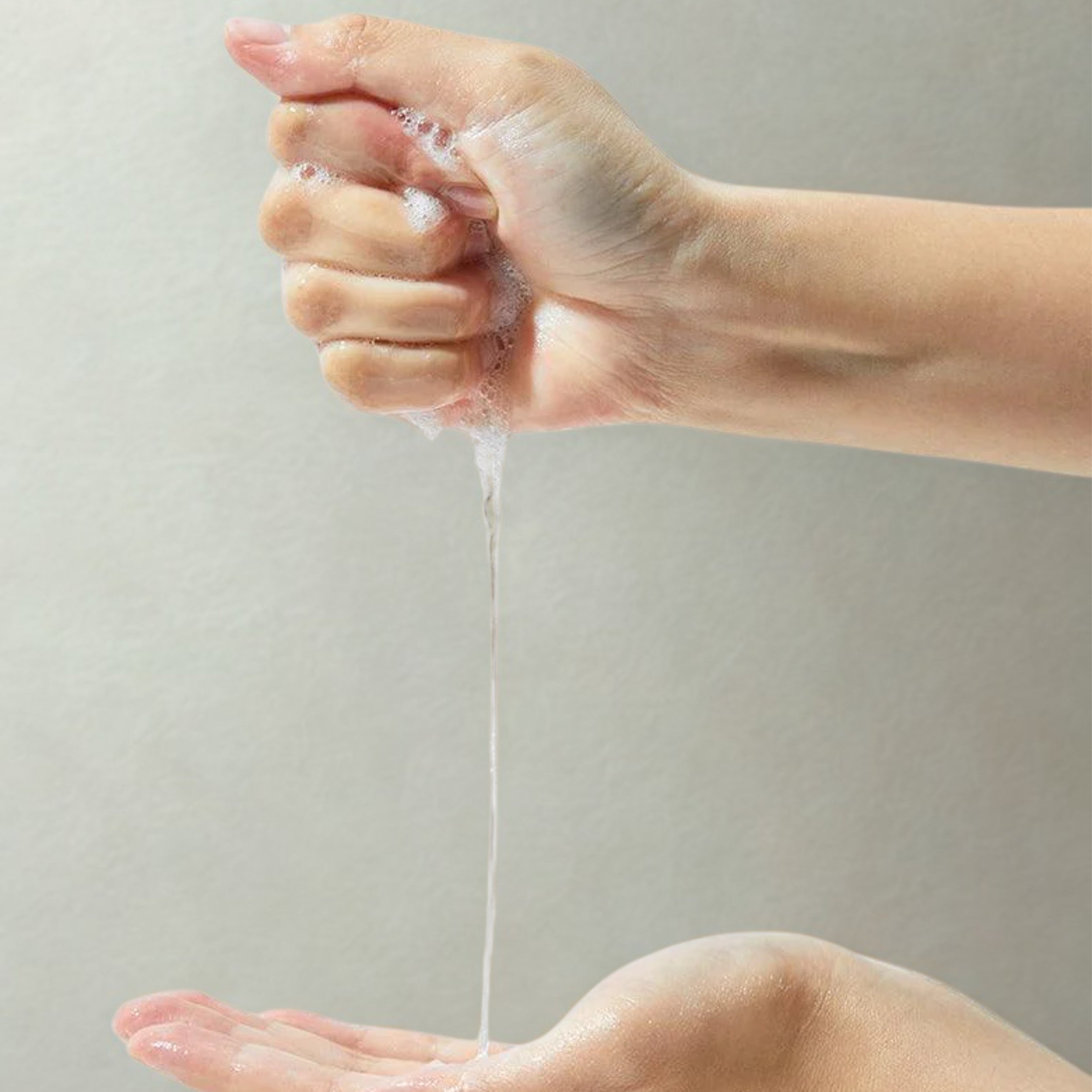 Hand washing with soap under running water against a neutral background