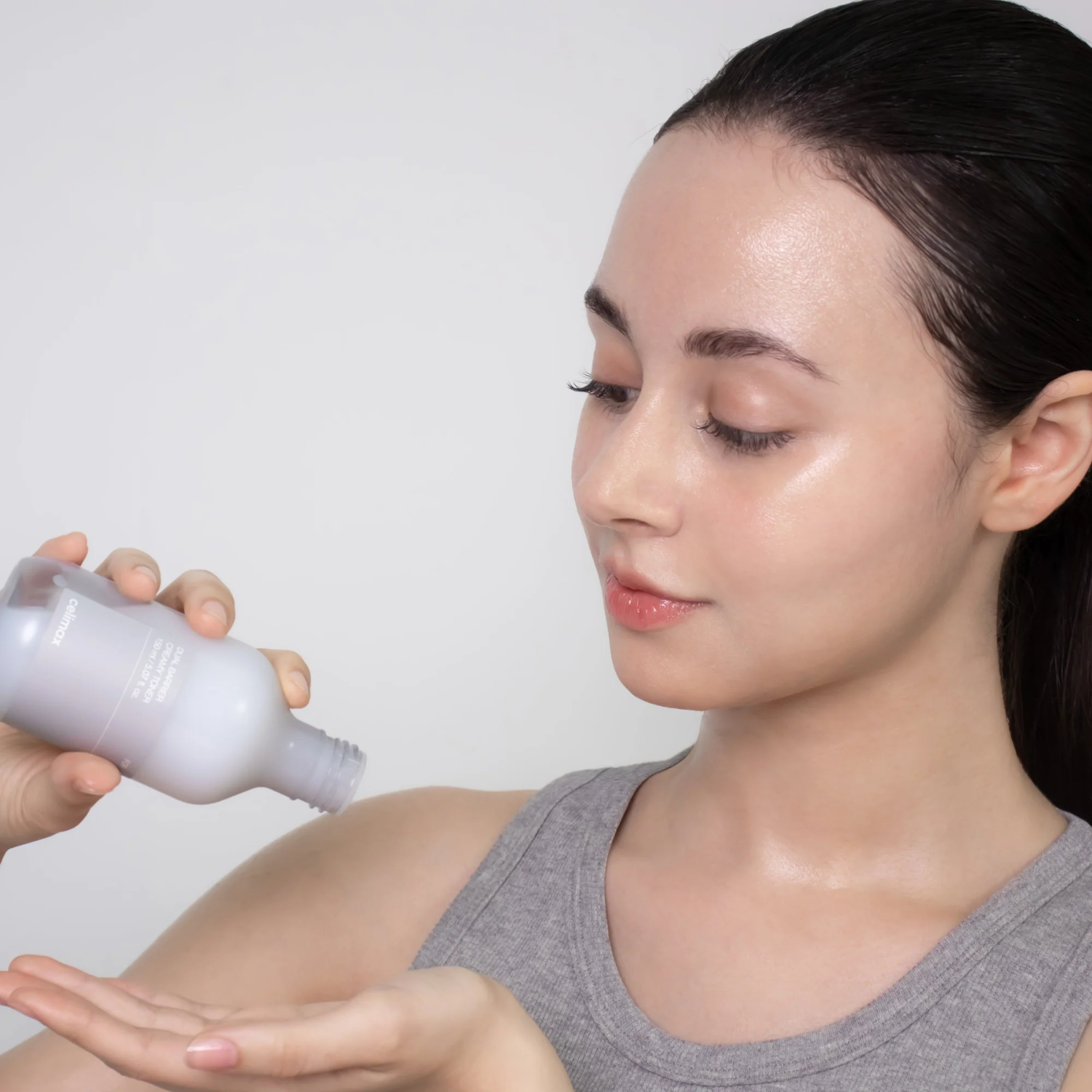Woman applying a white cream or lotion to her arm with a neutral background