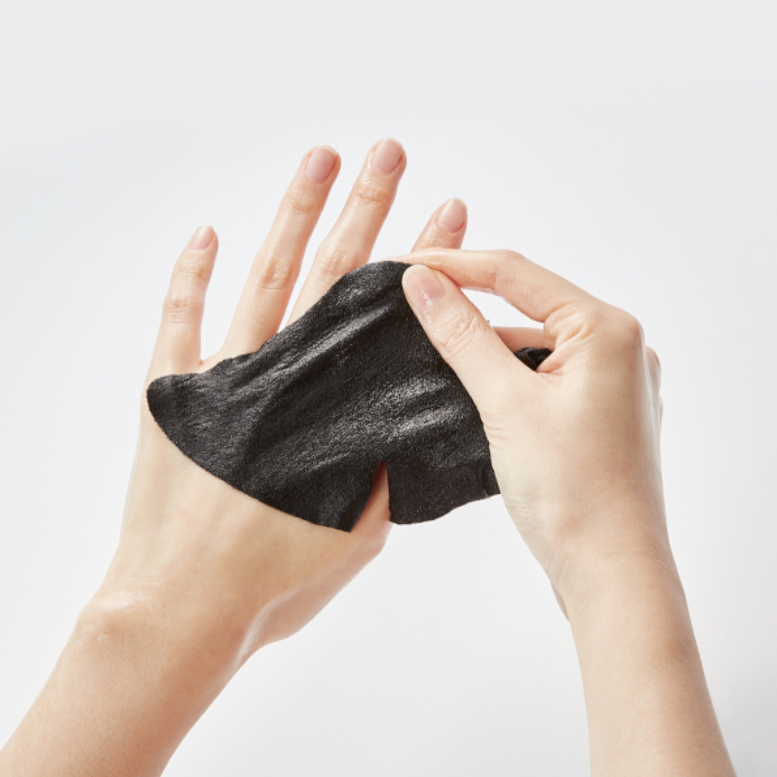 Person holding a black charcoal mask between their fingers against a light background