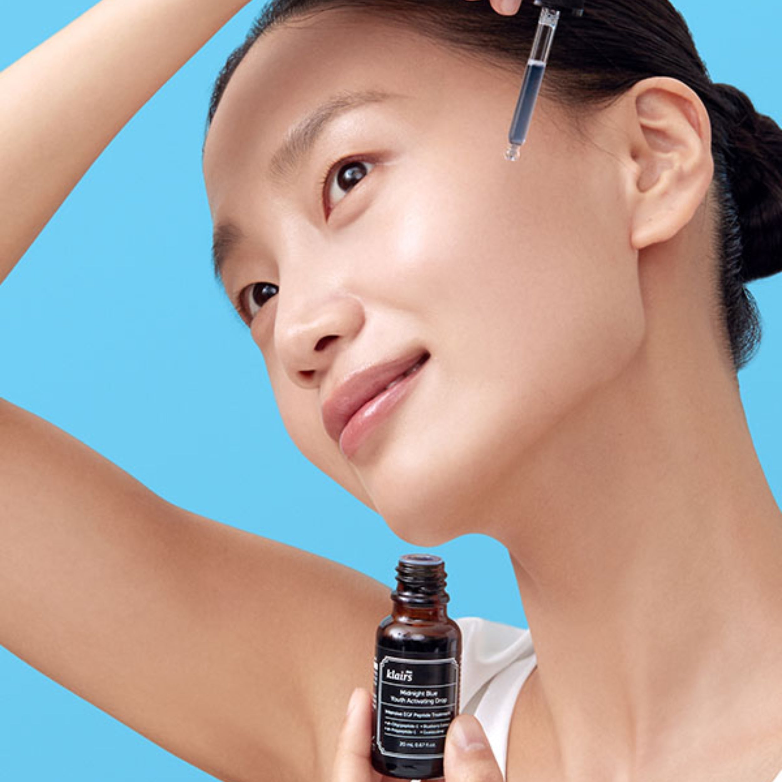 Woman applying skincare product with a dropper against a blue background