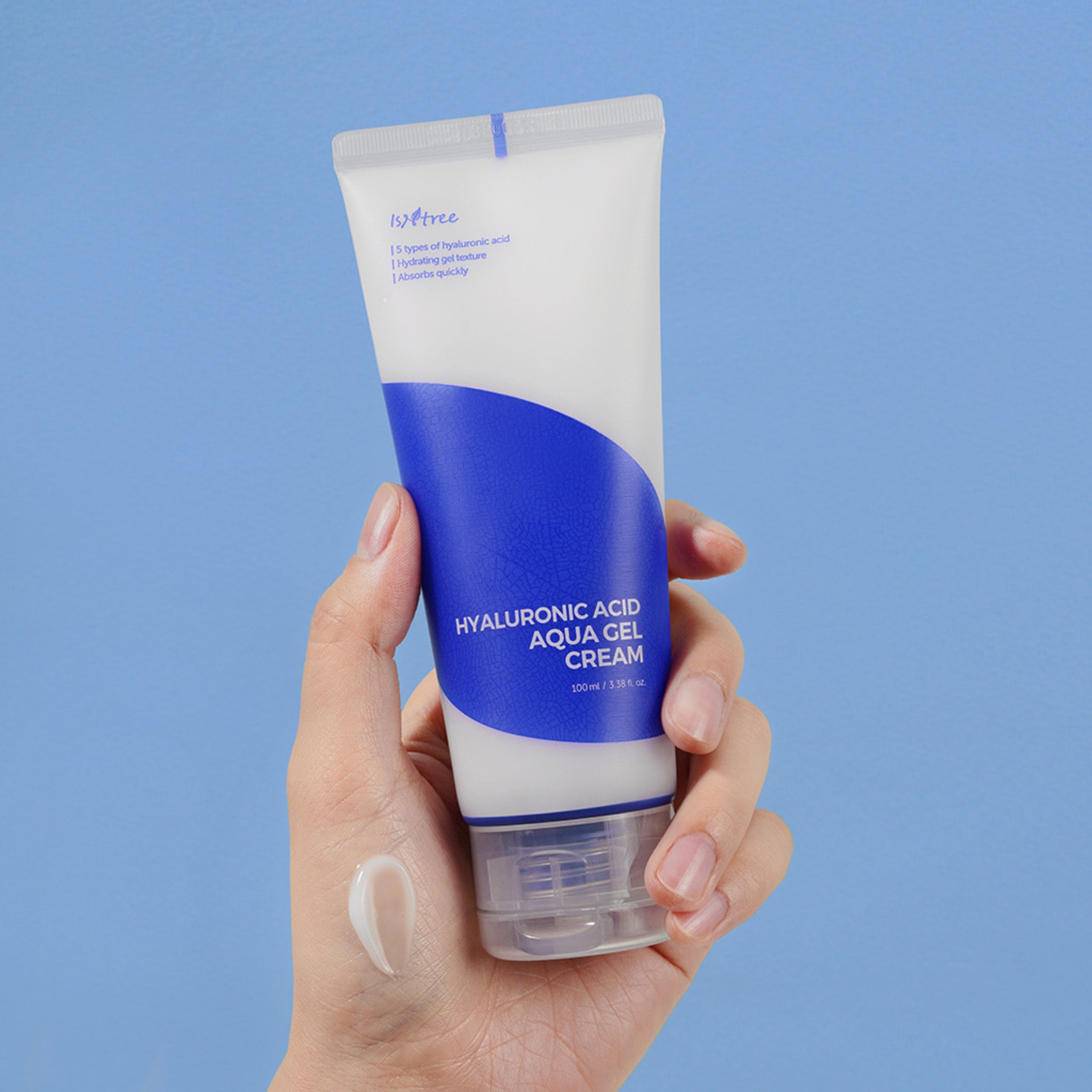 Hand holding a tube of hyaluronic acid aqua gel cream against a blue background