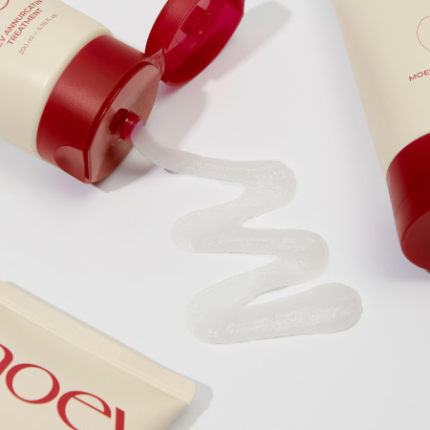 Red and beige treatment bottles with a white cream being squeezed out on a white background