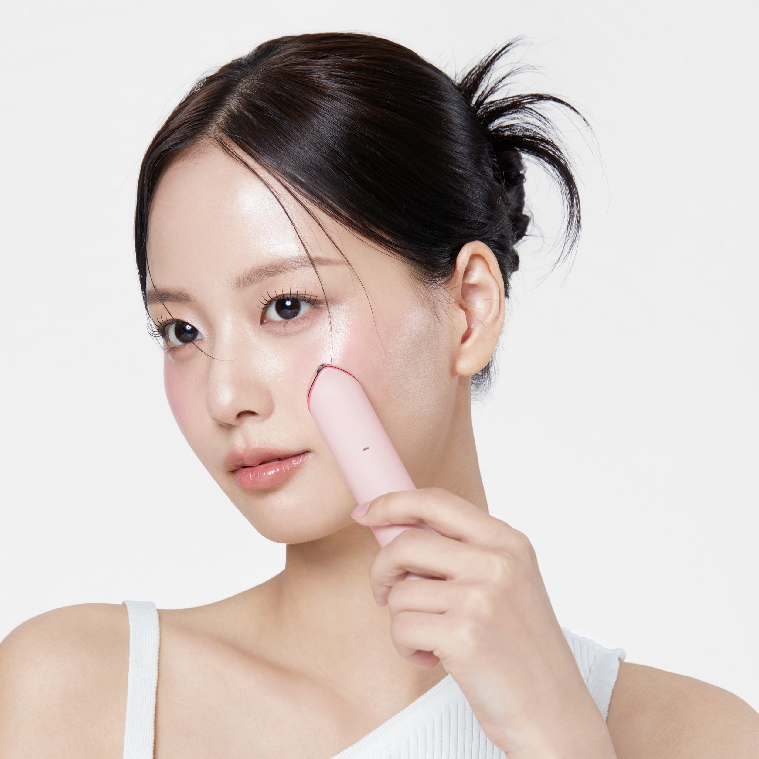 Woman using a pink facial cleansing brush on a white background