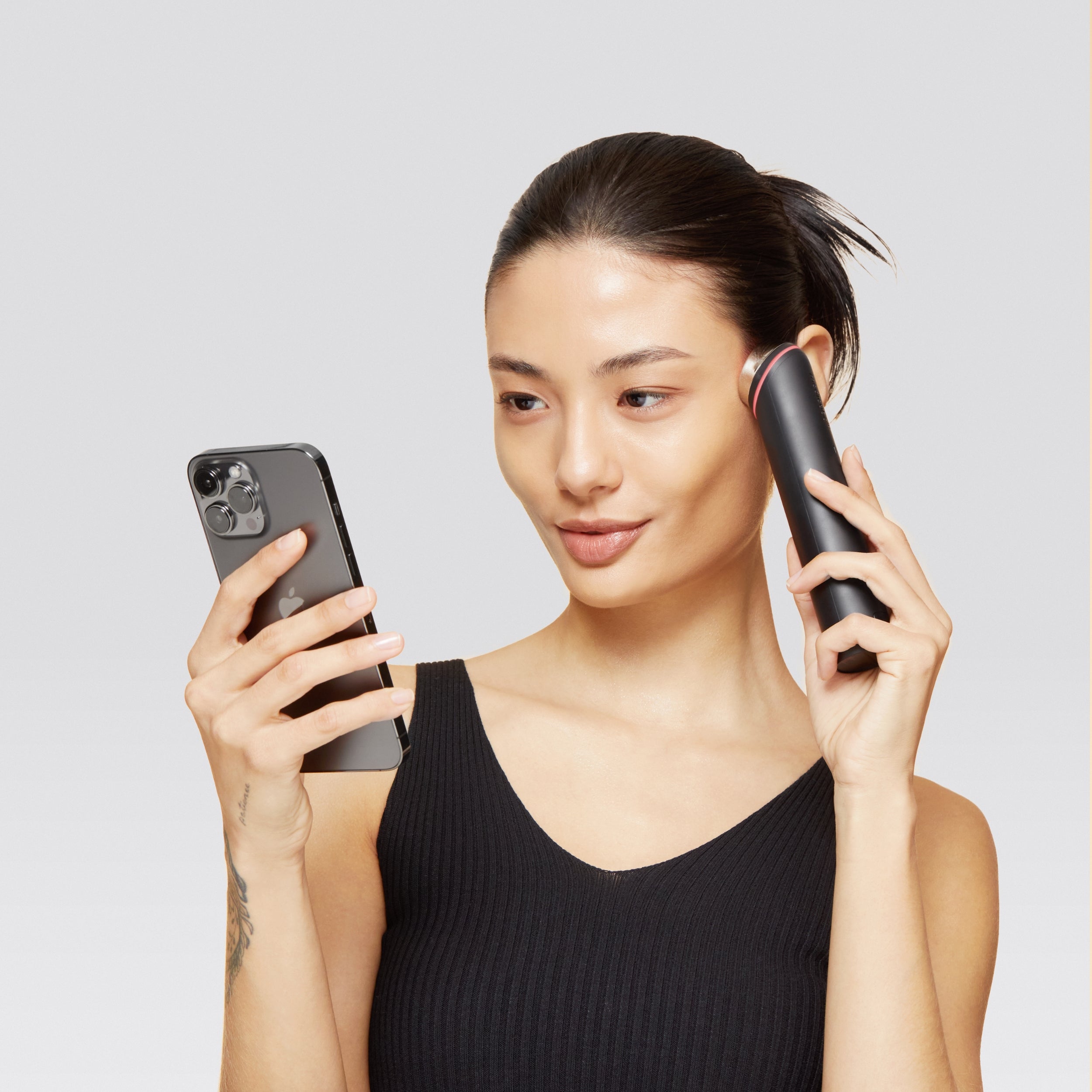 Woman holding a phone and a hair styling tool against a light gray background