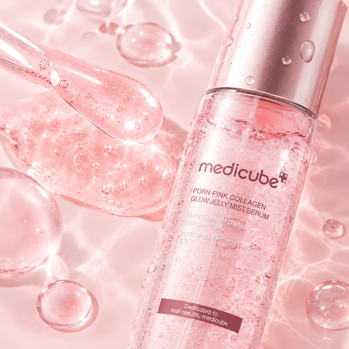 Medicube PDRN PINK Collagen Glow Jelly Mist Serum in a clear cylindrical bottle with a metallic pink cap, surrounded by pink translucent gel, droplets, and water-like reflections on a soft pink background.