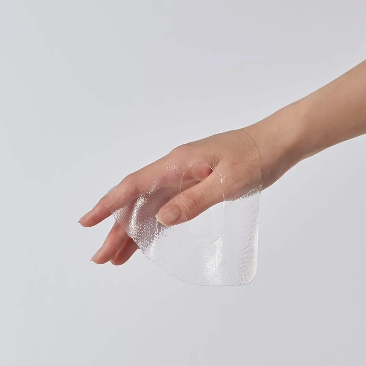 A hand holding a transparent, textured adhesive patch against a plain light gray background.