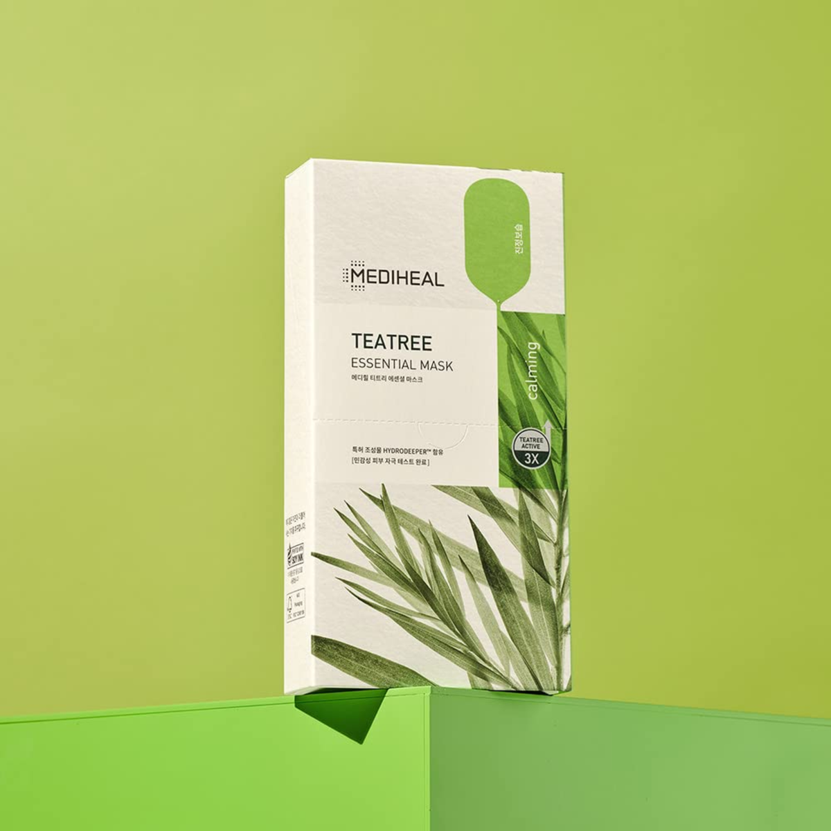 Mediheal Teatree Essential Mask packaging box, featuring a white and green design with a teardrop-shaped cutout window, set against a matching light green background.