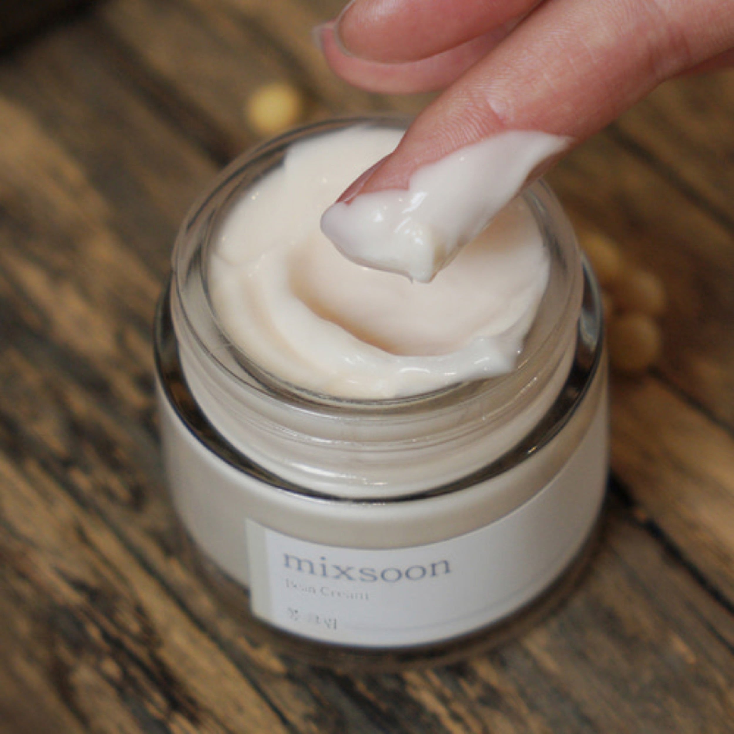 Hand applying cream from a jar labeled 'mixsoon' on a wooden surface