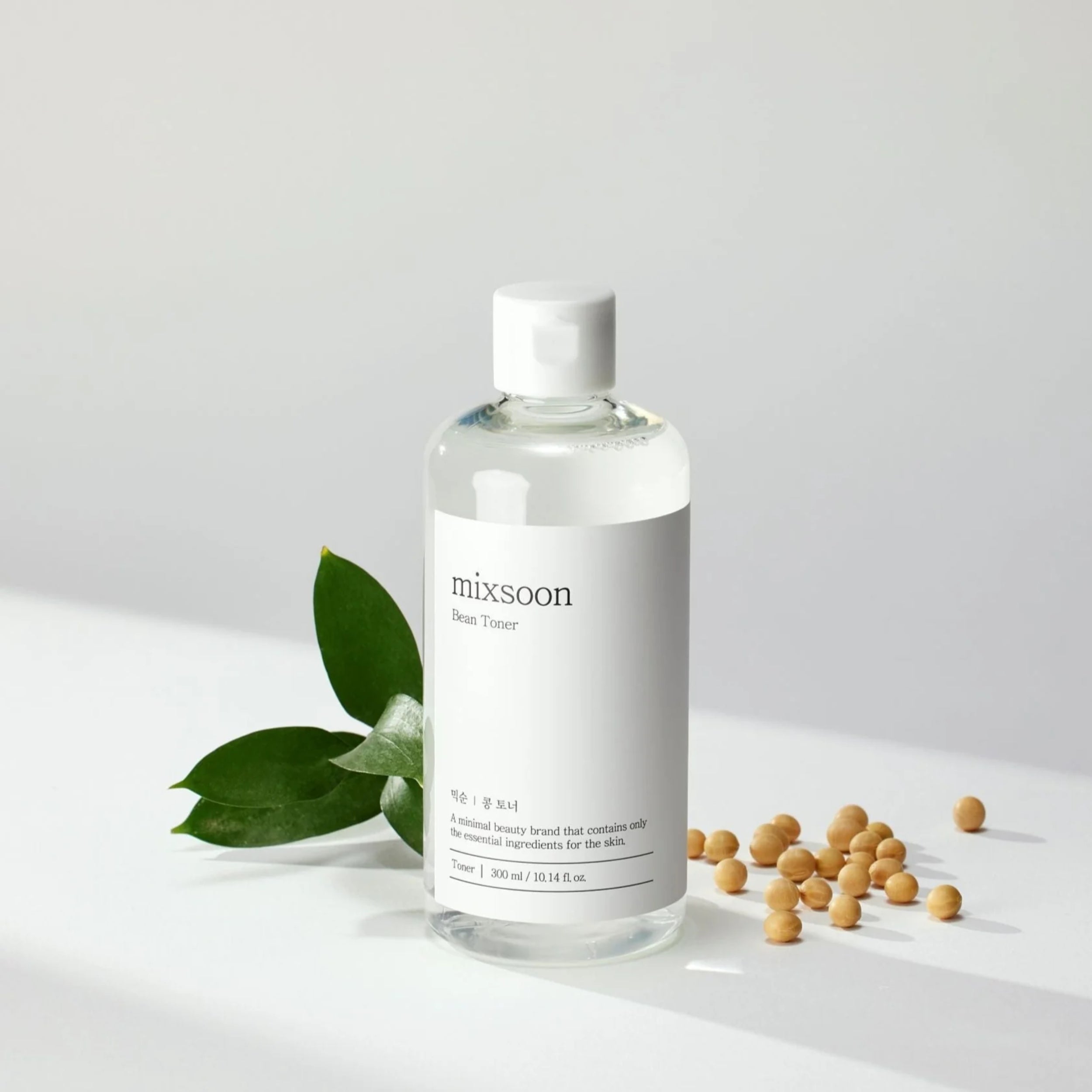 Clear bottle of 'mixsoon' toner with green leaves and small round objects on a light gray background
