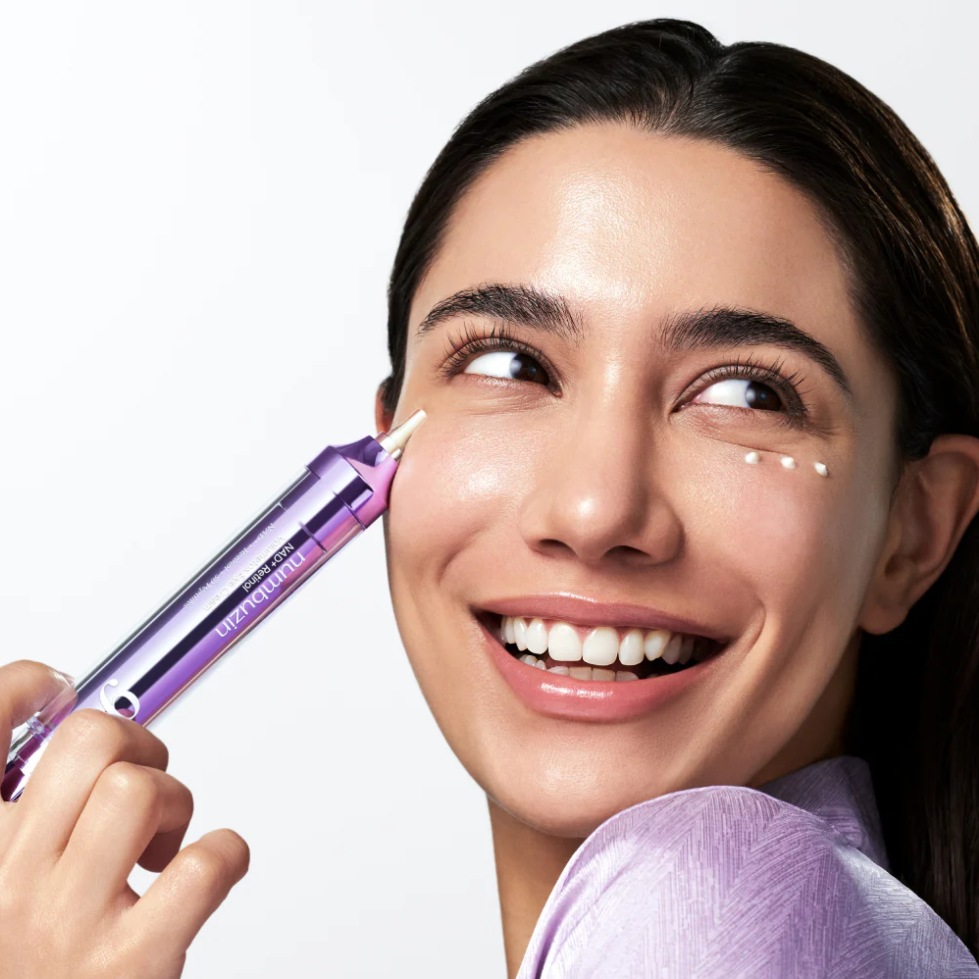 Woman applying a cosmetic product to her face with a purple applicator.