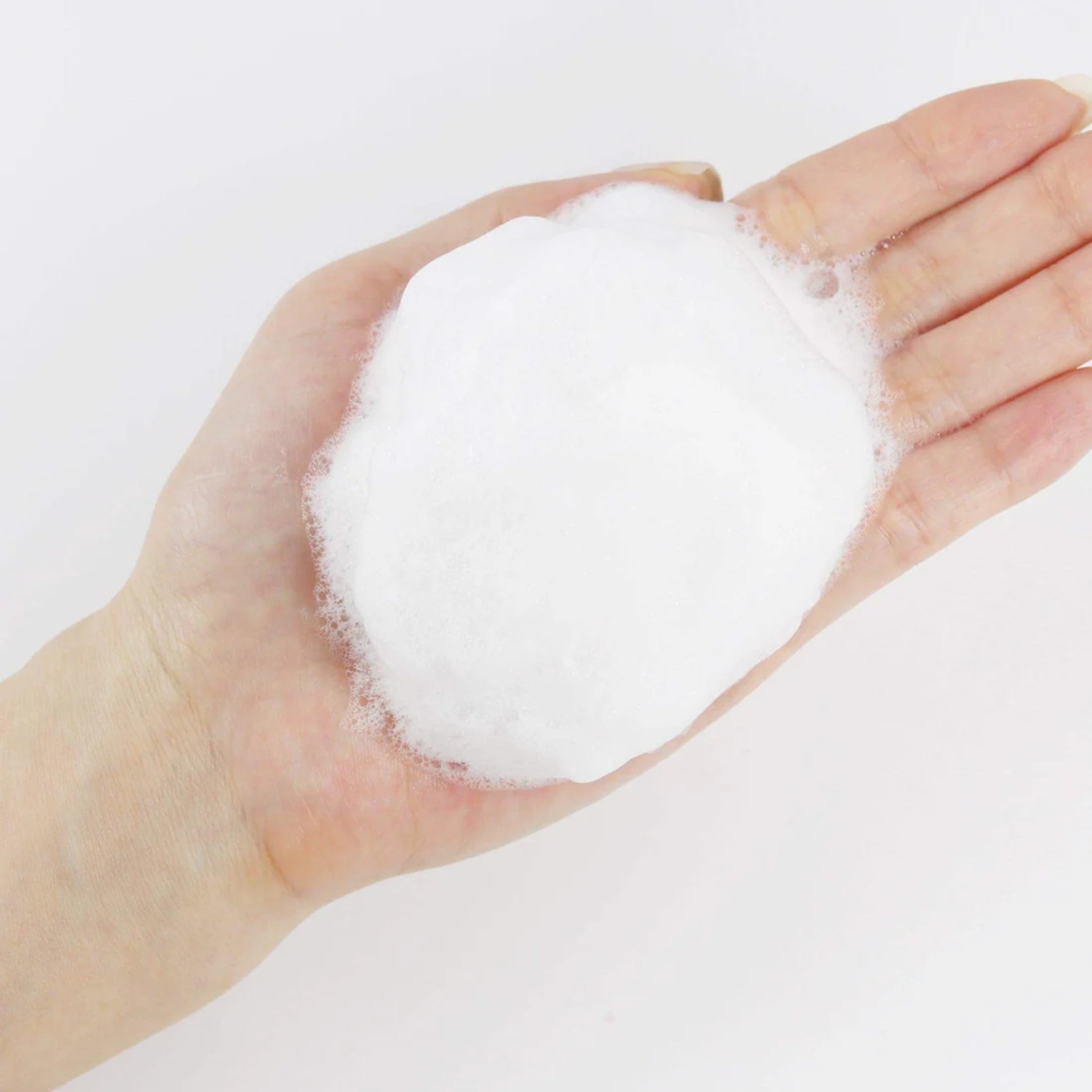 Hand holding a ball of white foam against a light gray background