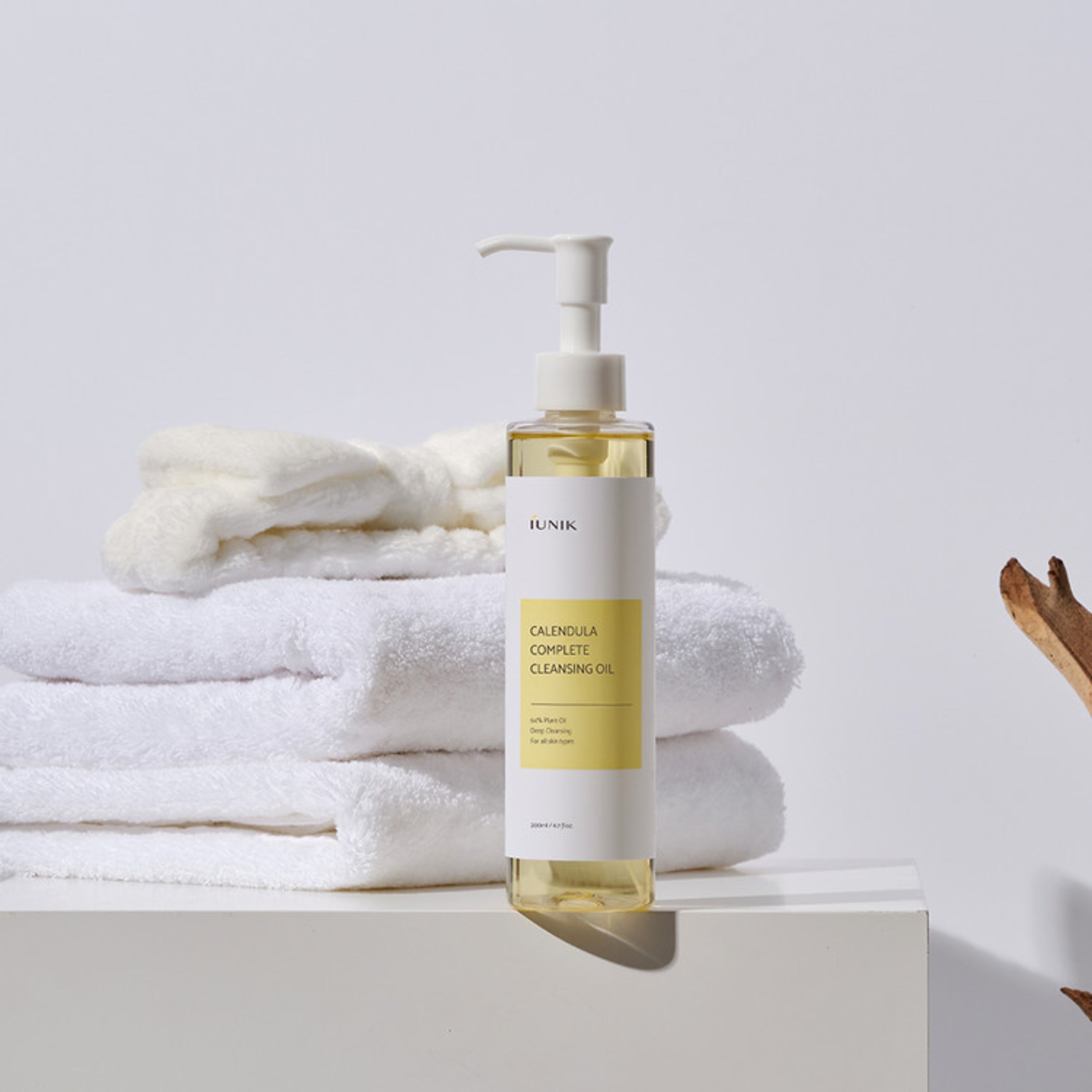 Bottle of IUNIK Calendula Complete Cleansing Oil on a white surface with towels in the background