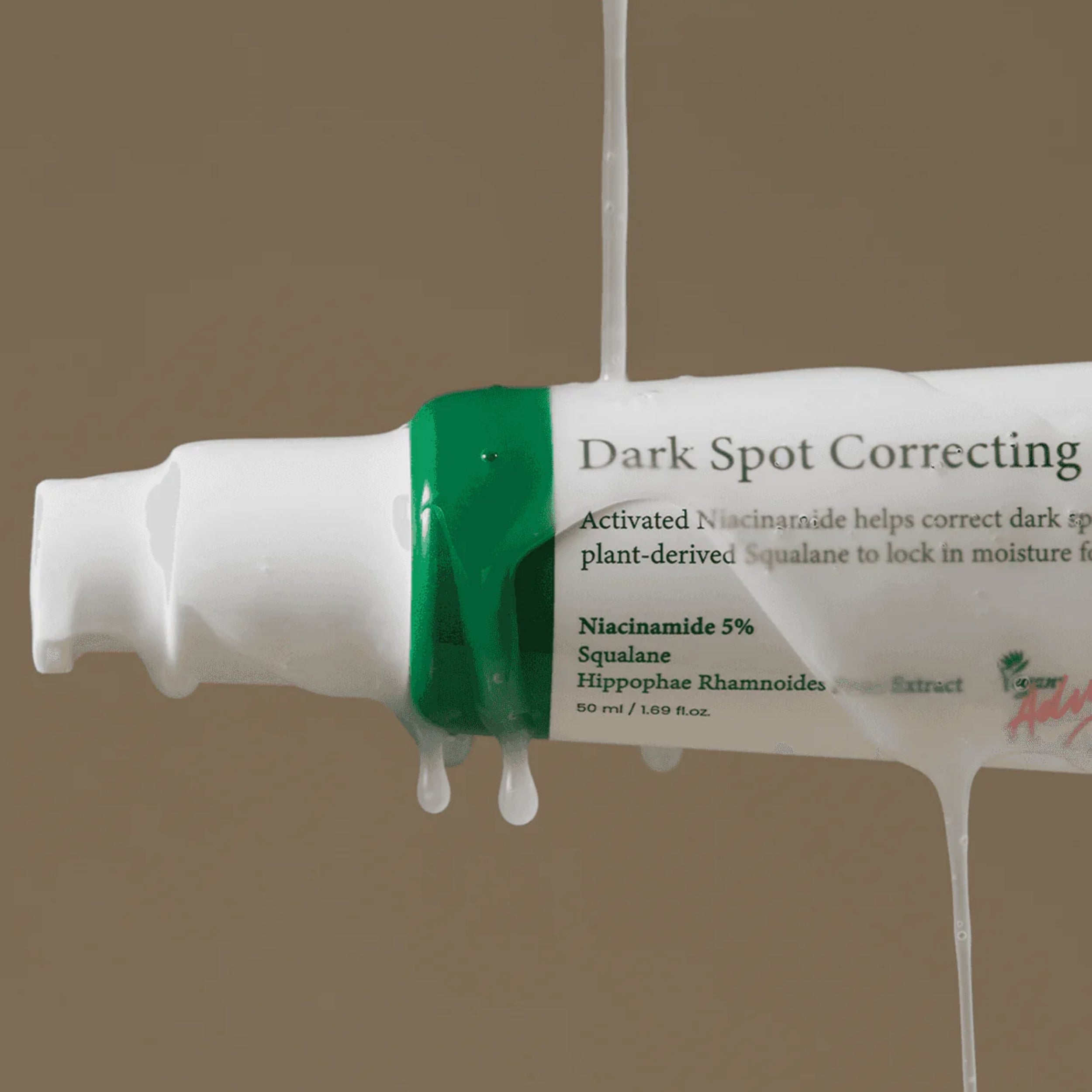 Tube of dark spot correcting cream with green applicator on a beige background