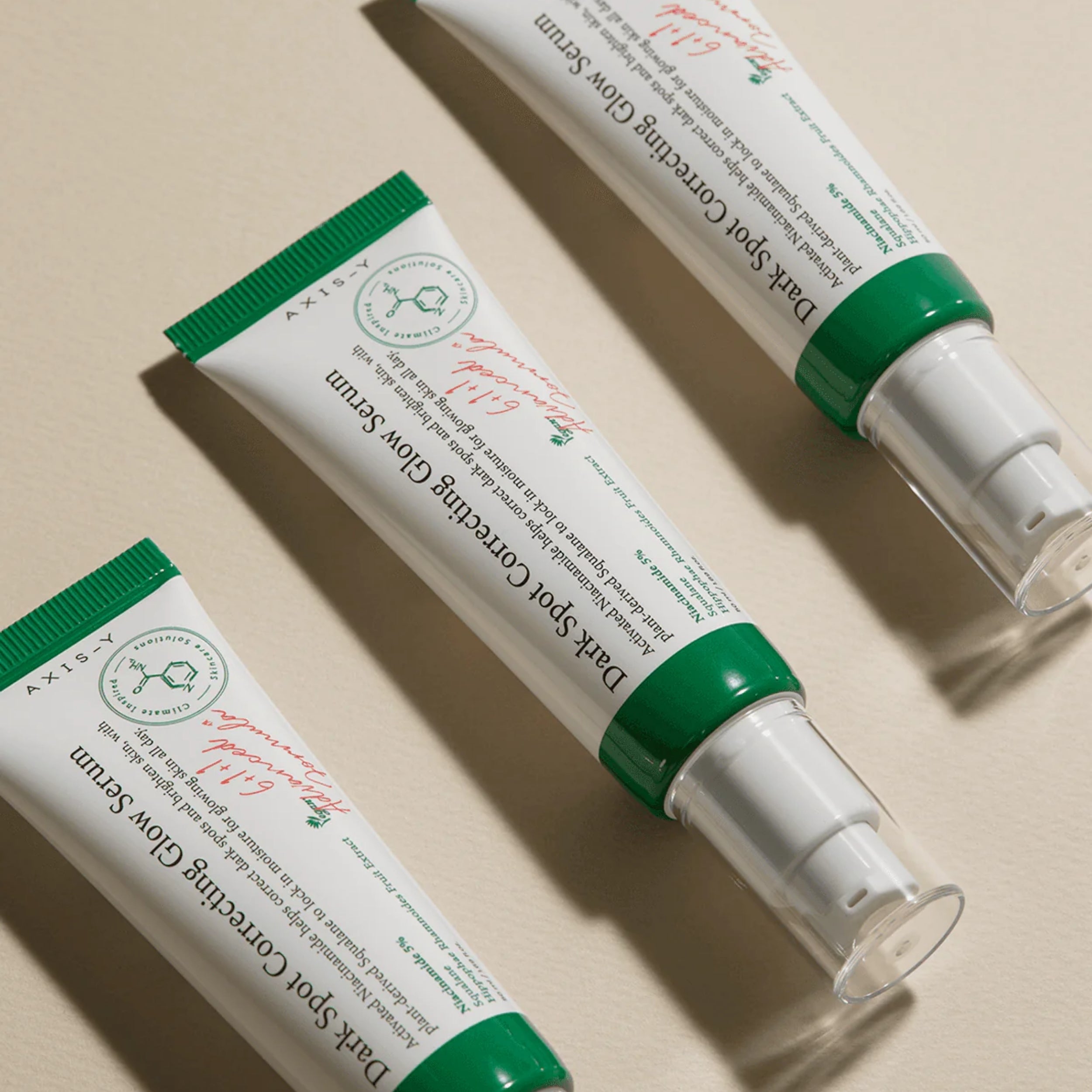 Two tubes of Dark Spot Correcting Glow Serum with green and white packaging on a beige background