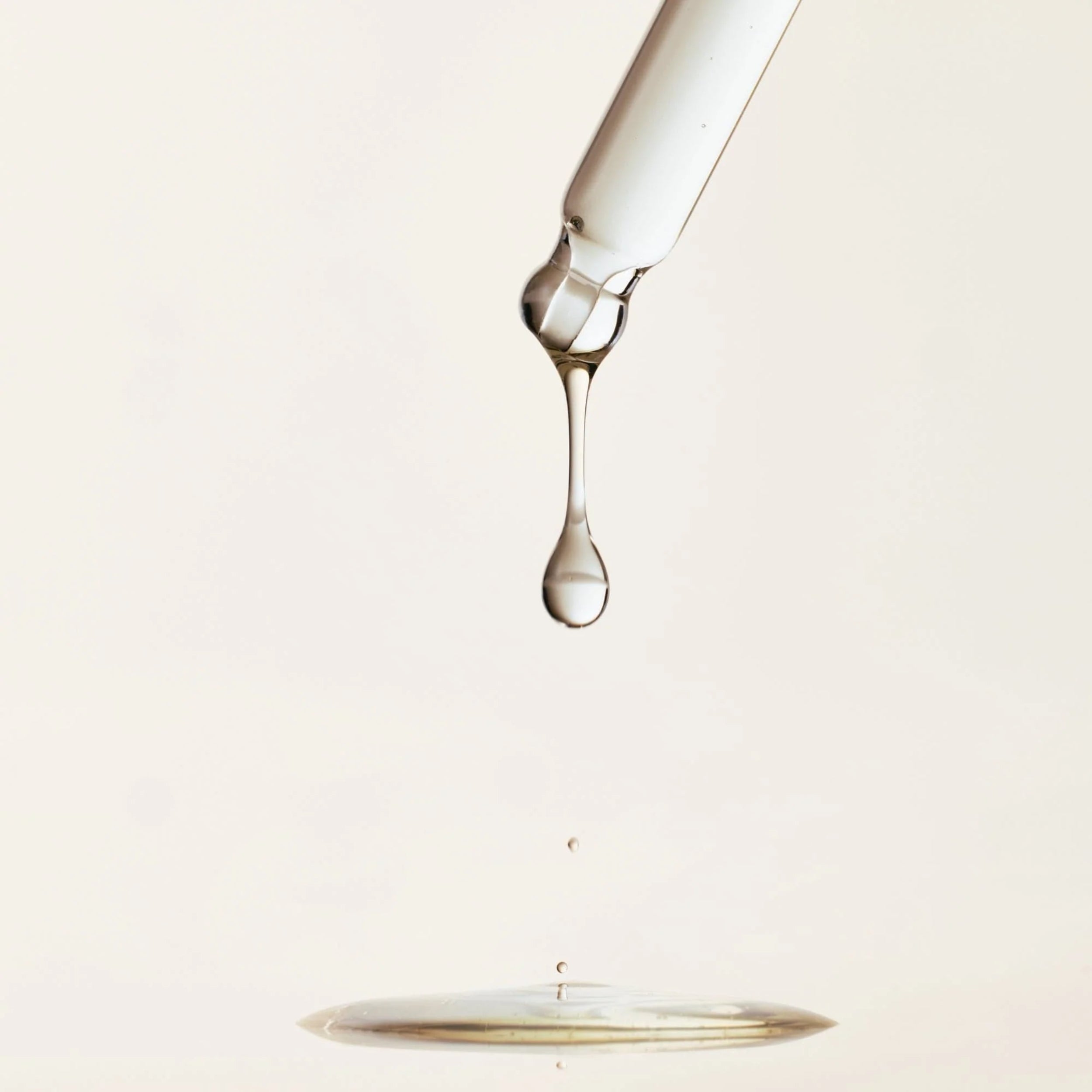 Glass bottle with a droplet of liquid on a light beige background