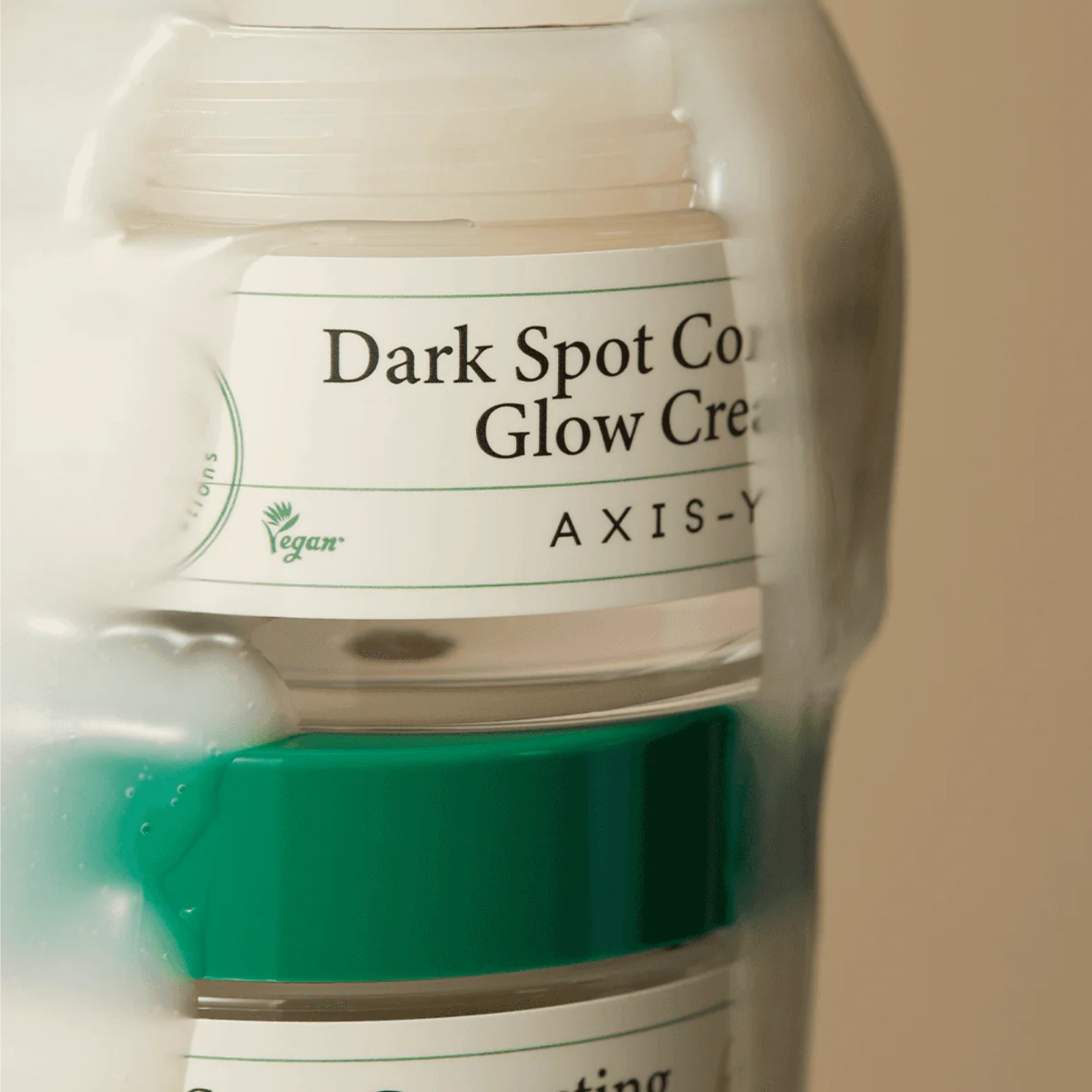 Jar of 'Dark Spot Corrector Glow Cream' by AXIS-Y with a green cap on a beige background