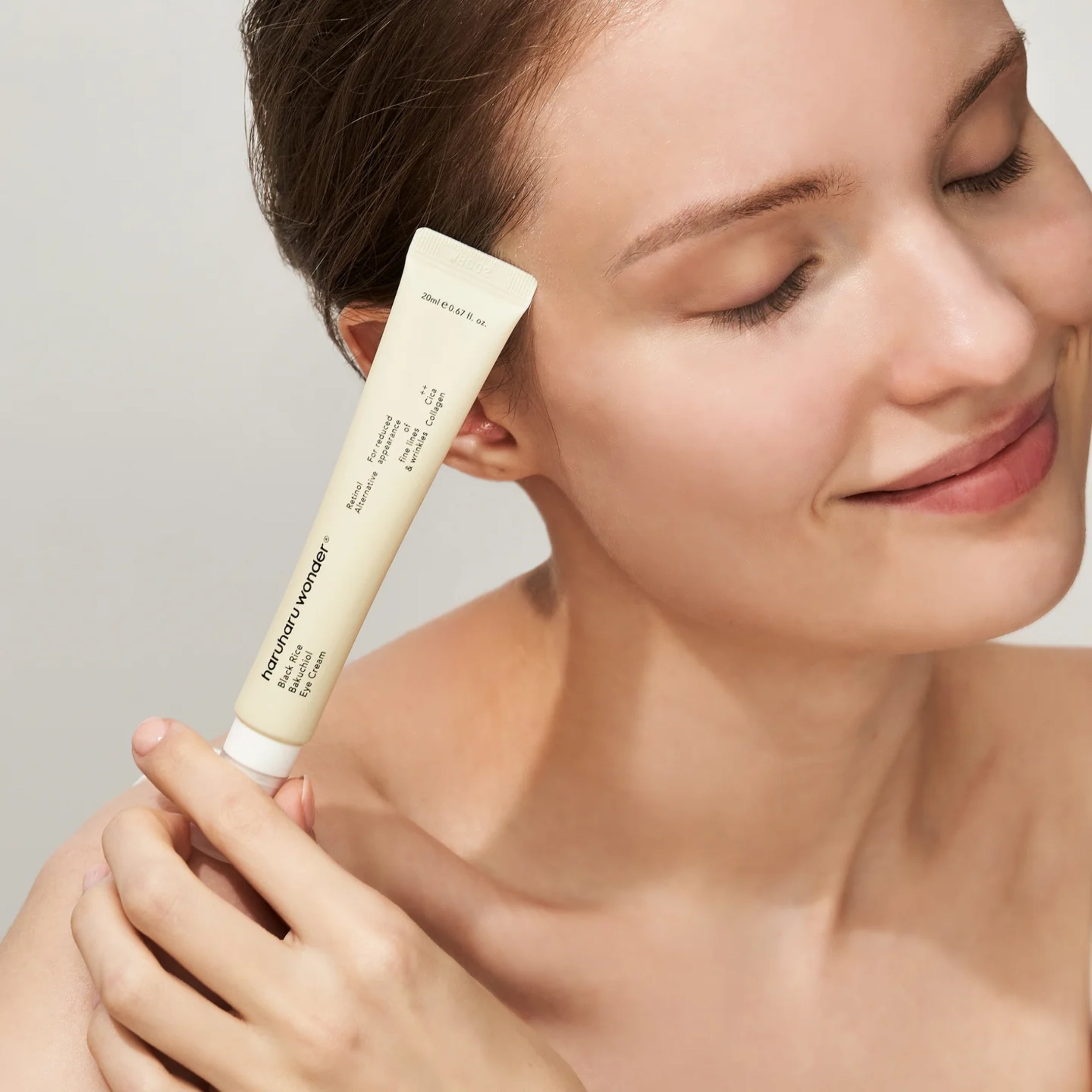 Woman holding a skincare product near her face against a neutral background