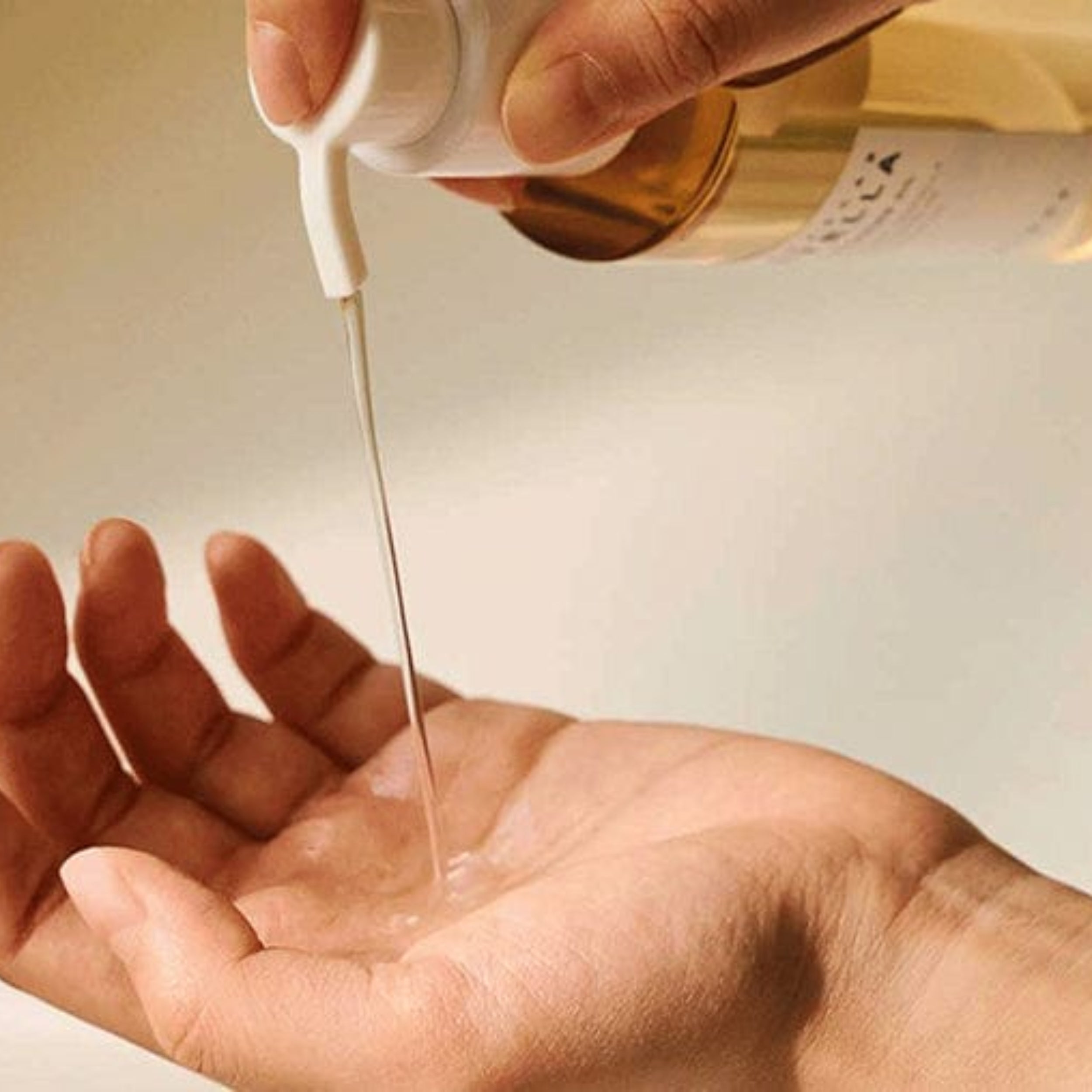 Hand pouring a clear liquid from a bottle into another container.