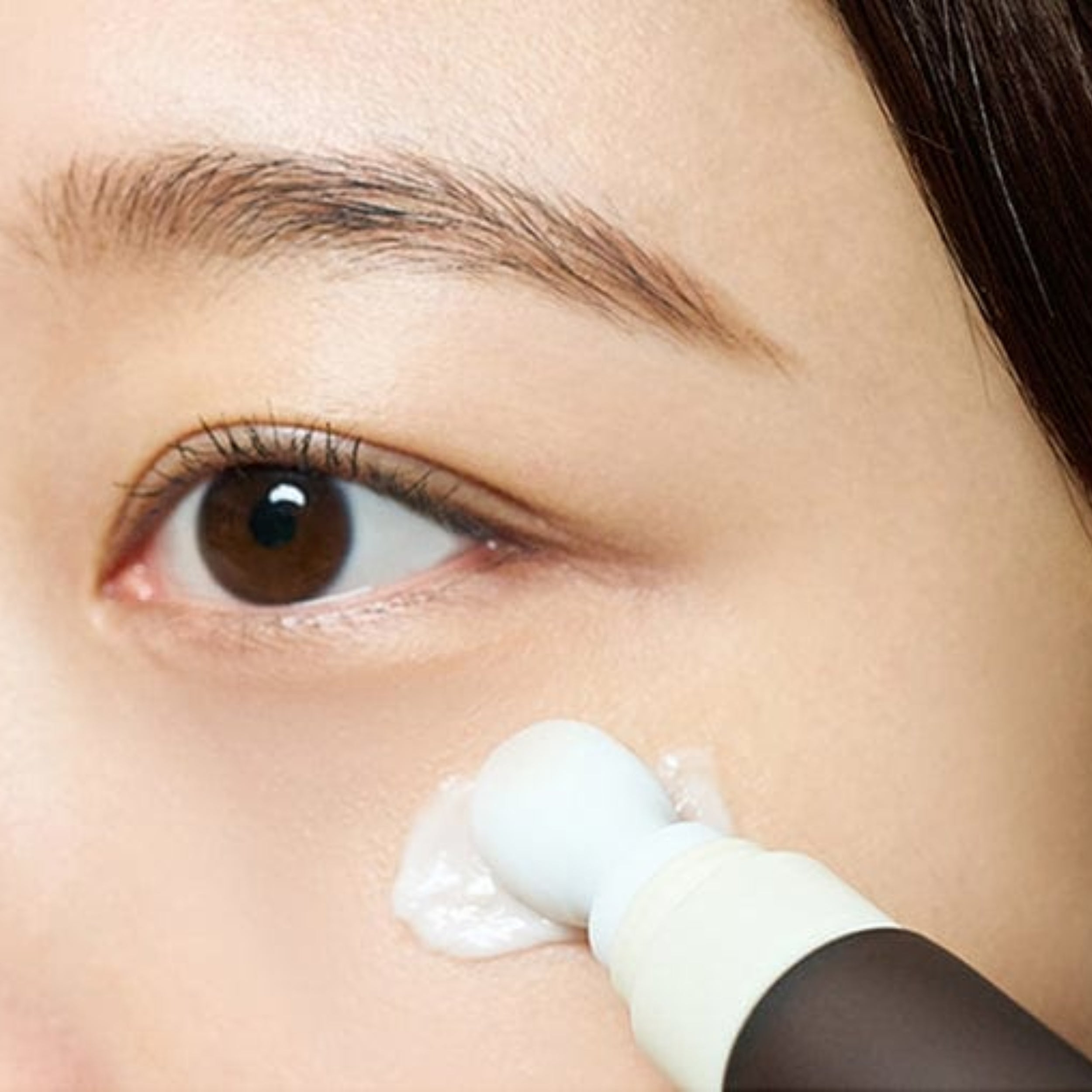 Close-up of a person applying cream under their eye with a brush.