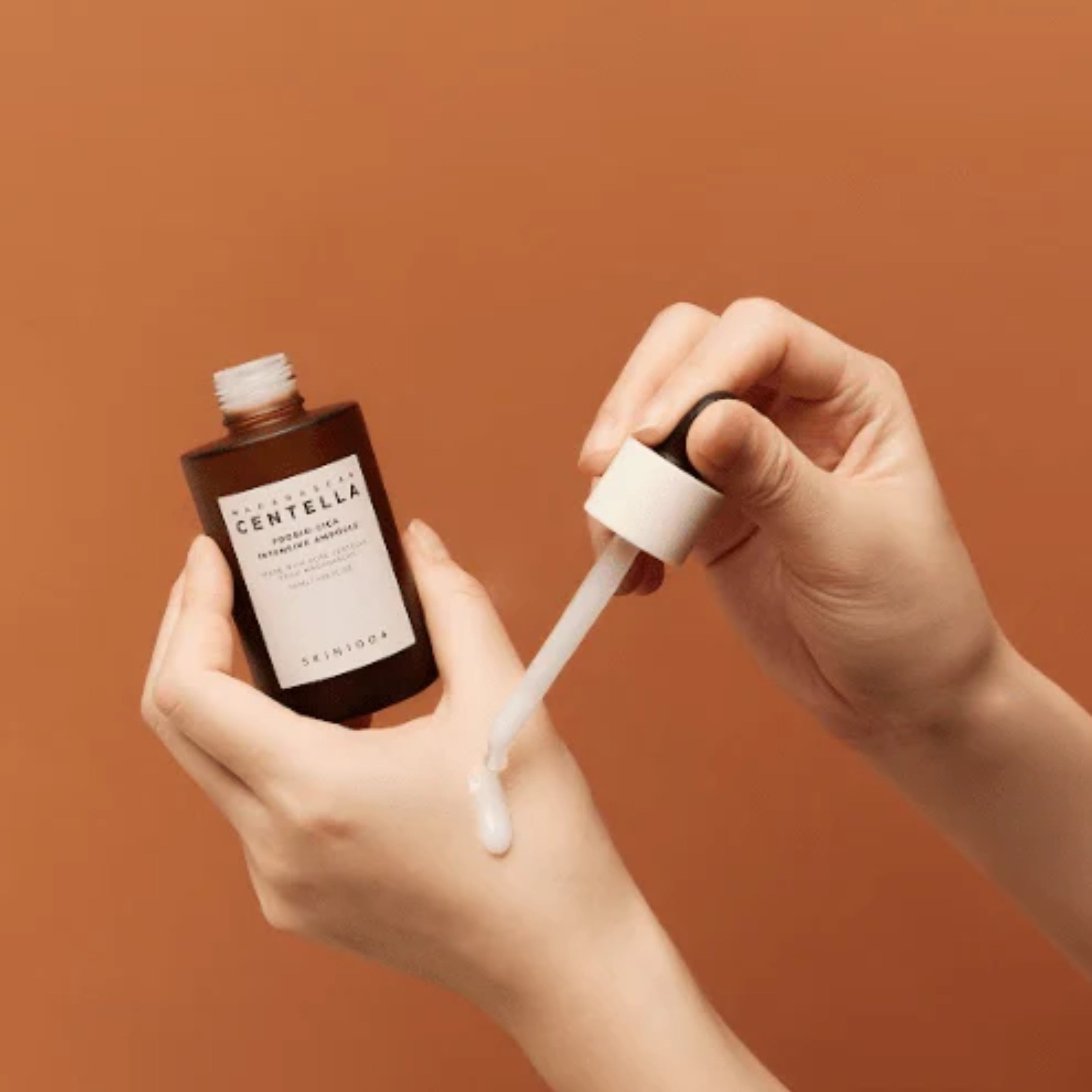 Person holding a bottle of Skinfood Centella and a dropper with a brown background