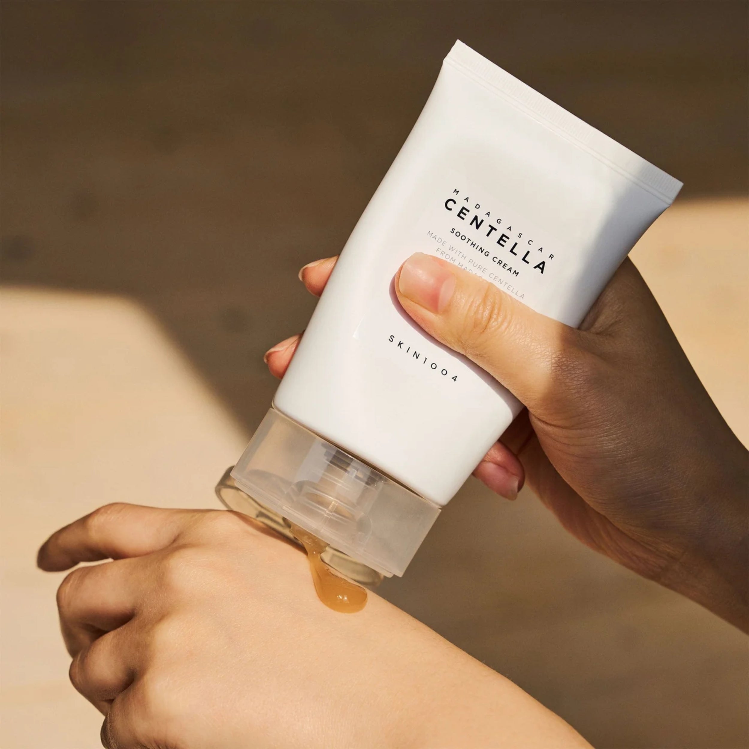 Hand applying Centella Asiatica skincare cream to wrist with a blurred background