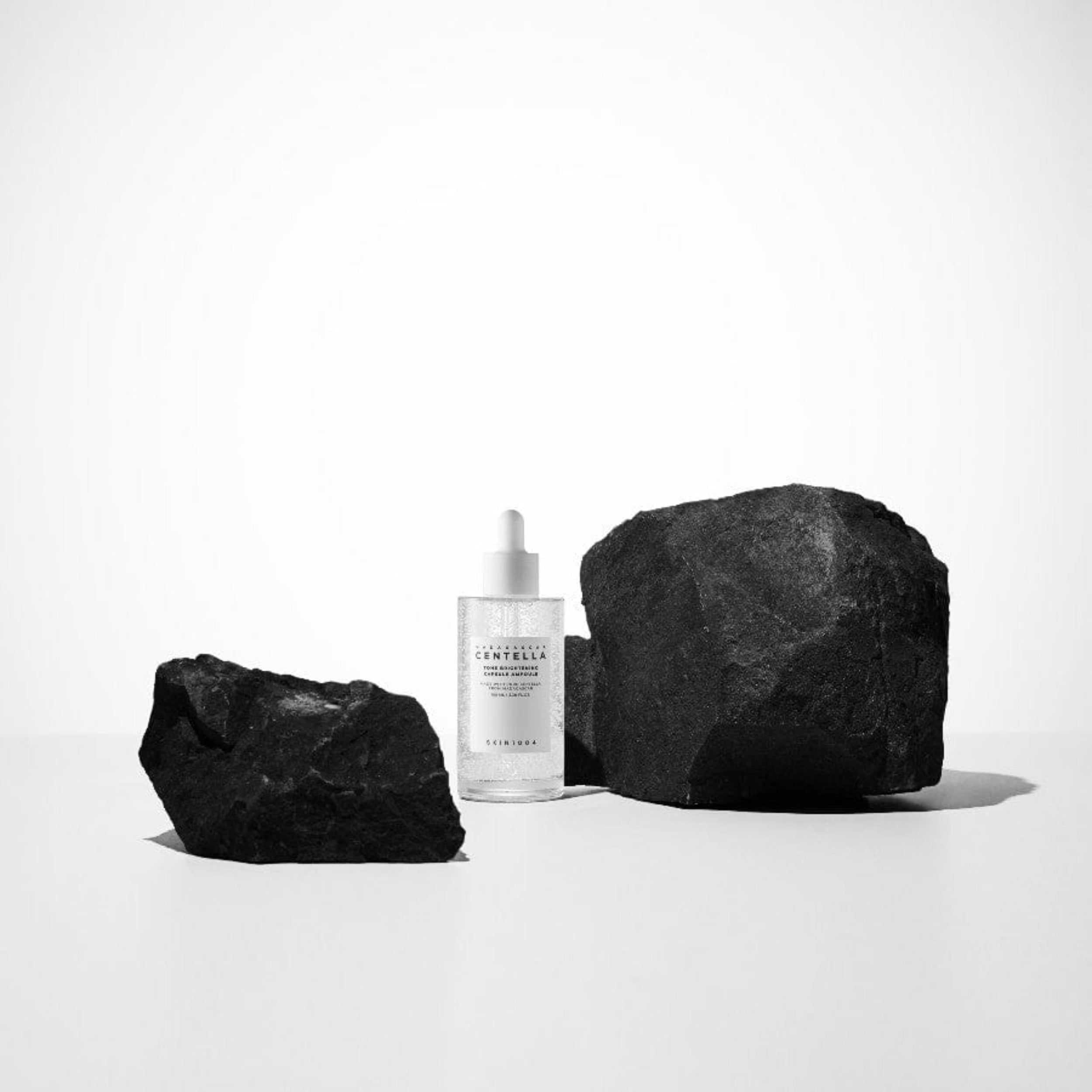Skincare bottle with two large black stones on a white background