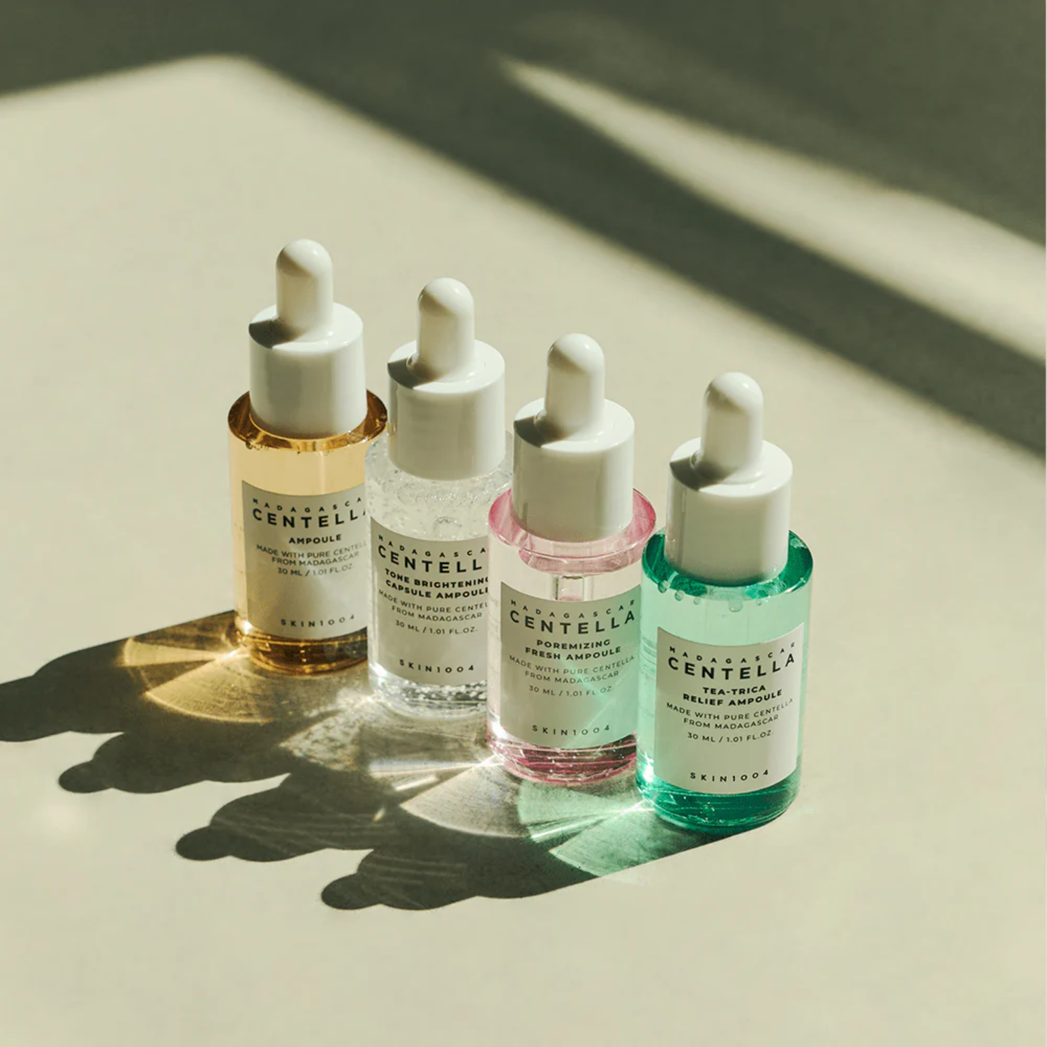 Four skincare dropper bottles with different colored liquids on a light surface.