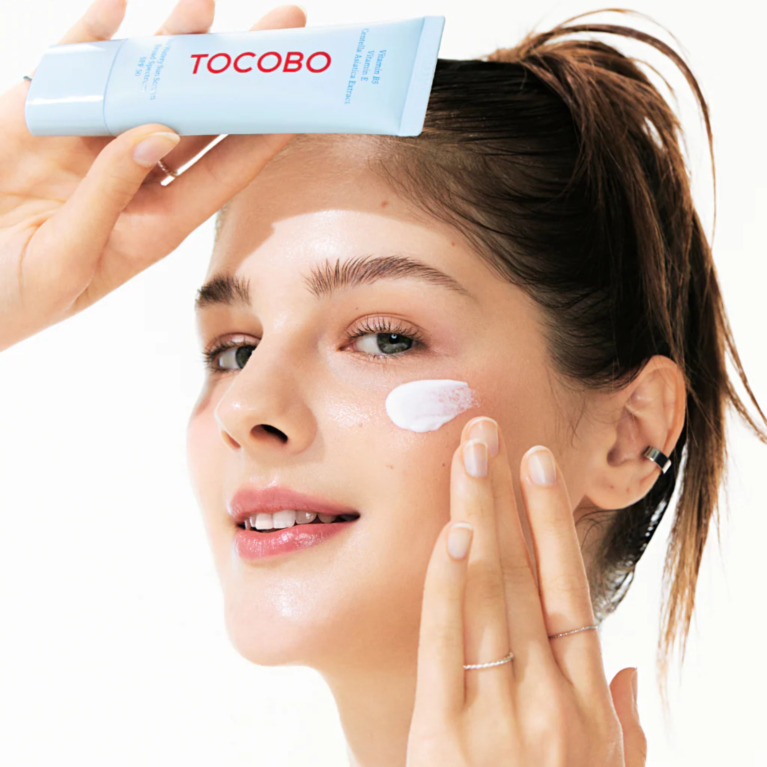 Woman applying Tocobo skincare product to her face with a white background