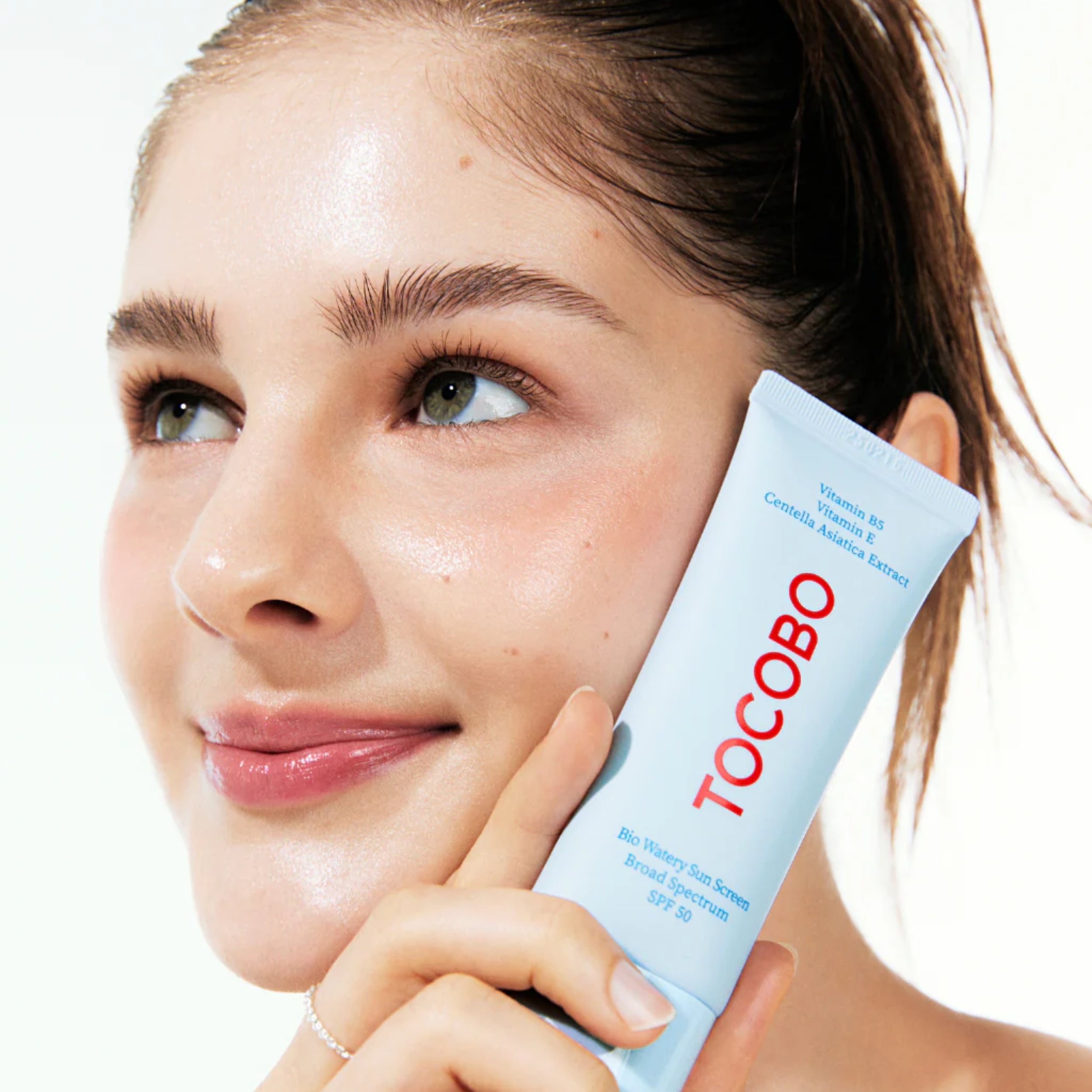 Woman holding a Tocobo skincare product with a close-up of her face.