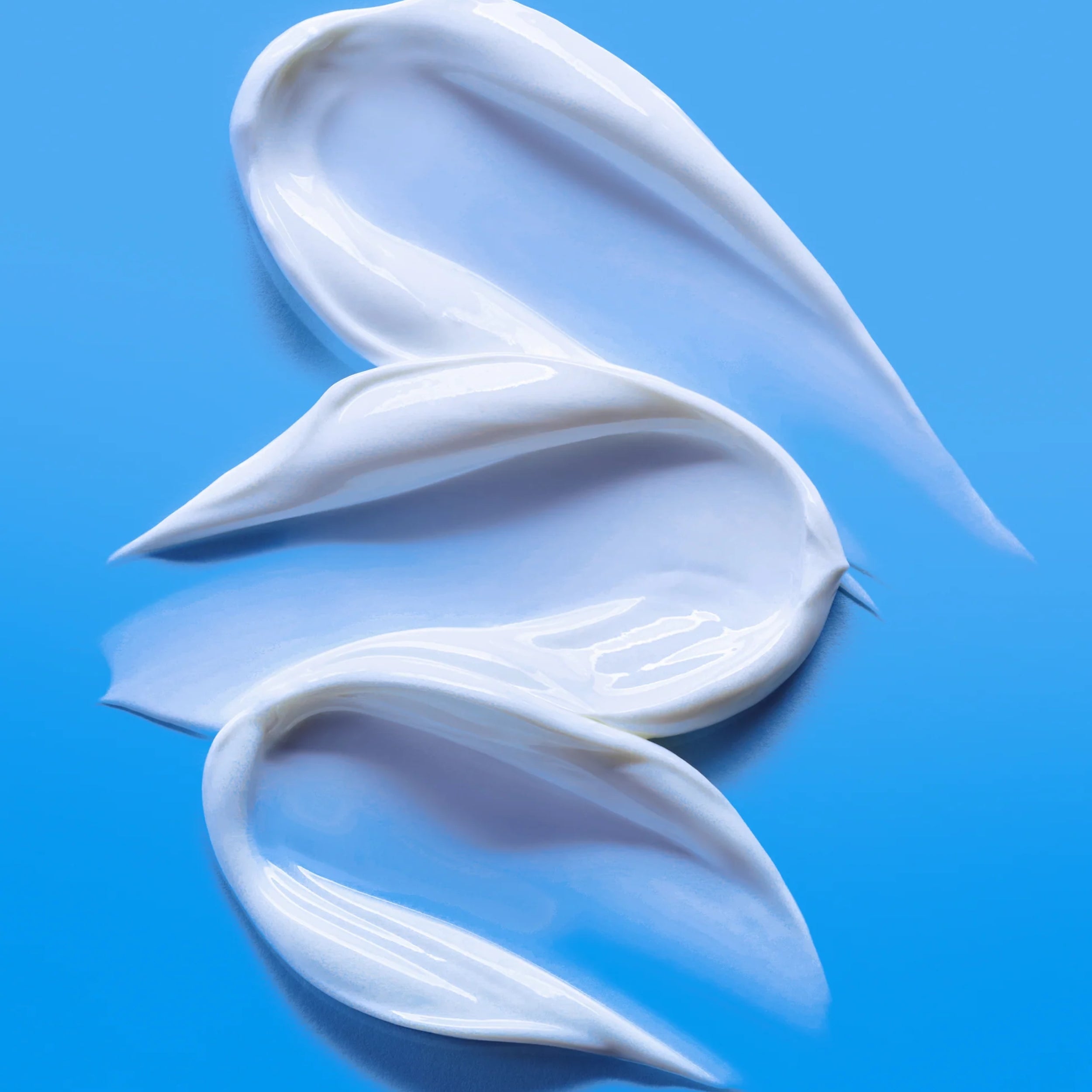 Three swatches of white cream on a blue background