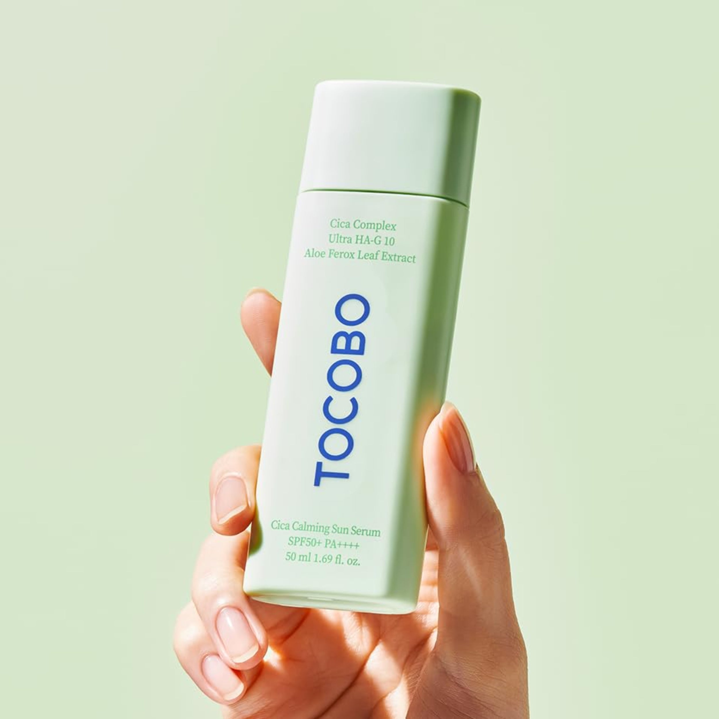 Hand holding a Tocobo skincare serum bottle against a light green background