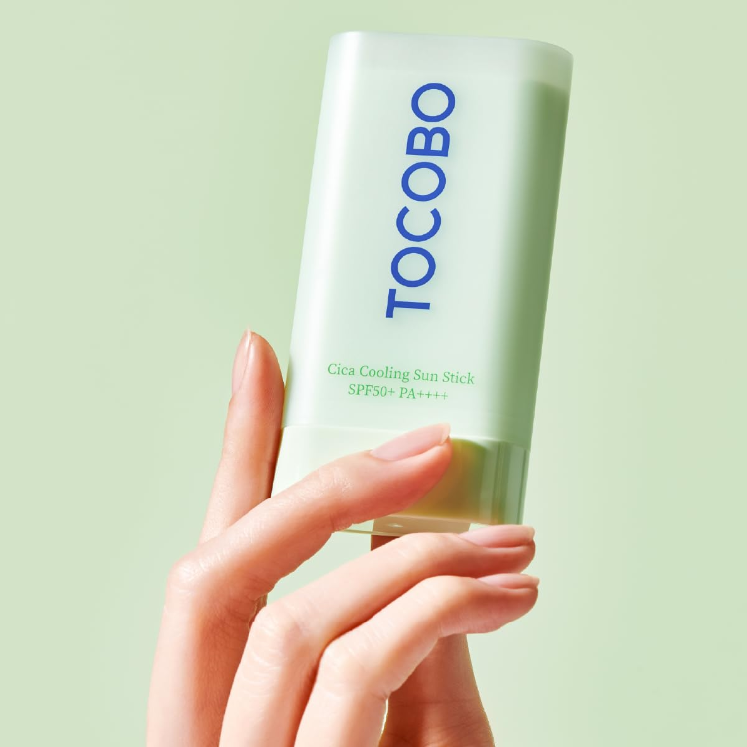 Hand holding a Tocobo sunscreen stick against a light green background