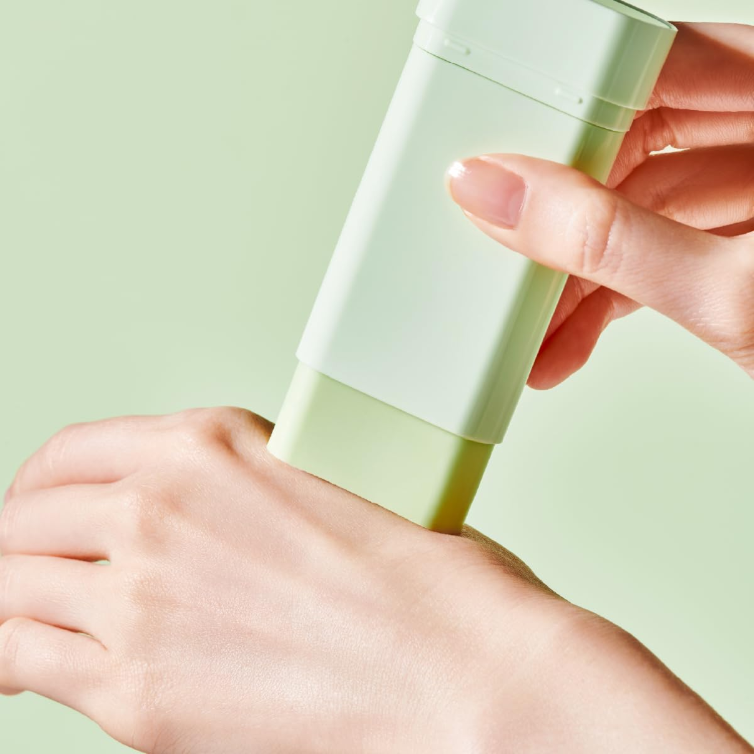 Hand applying a light green skincare product to another hand against a light green background