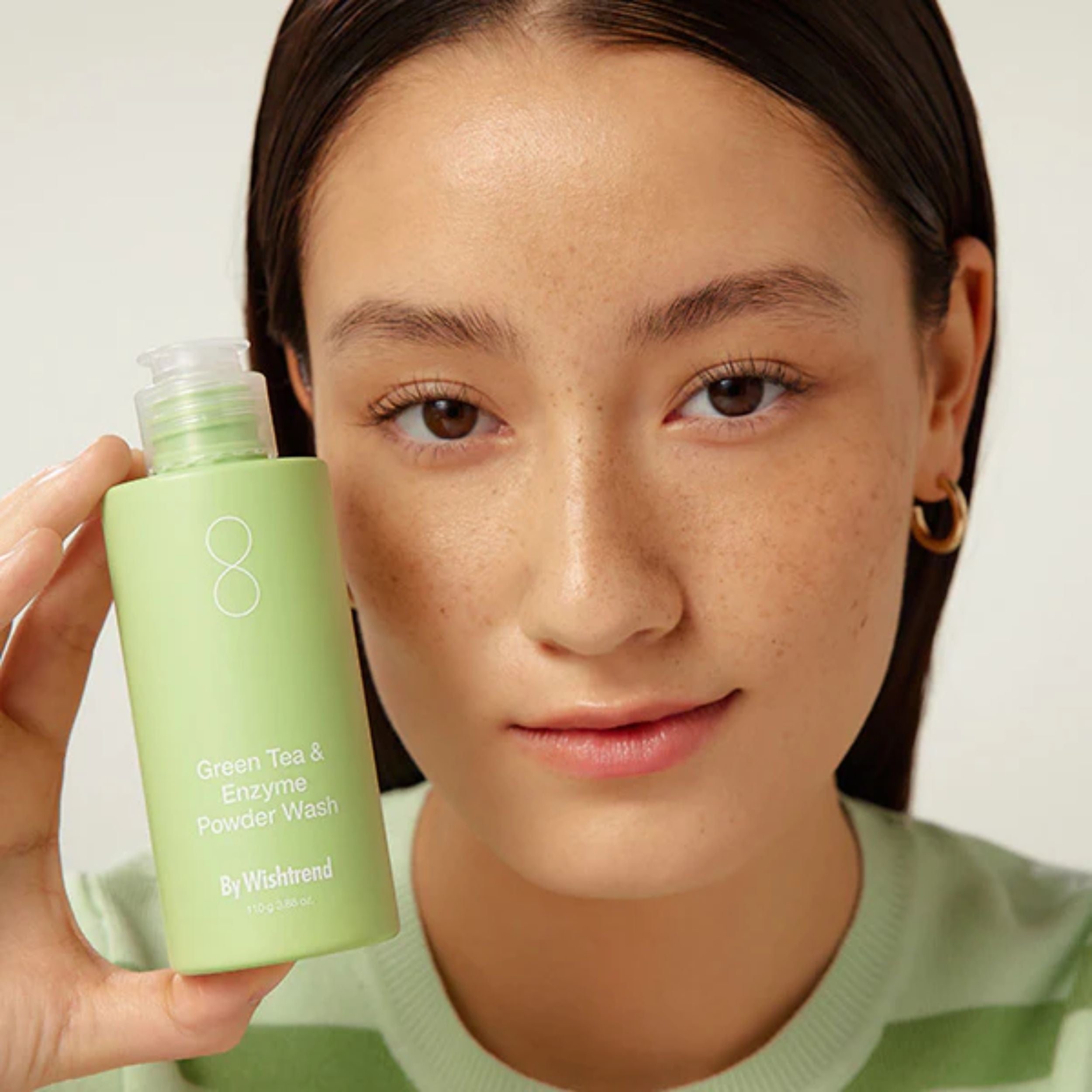 Person holding a green skincare product with a plain background