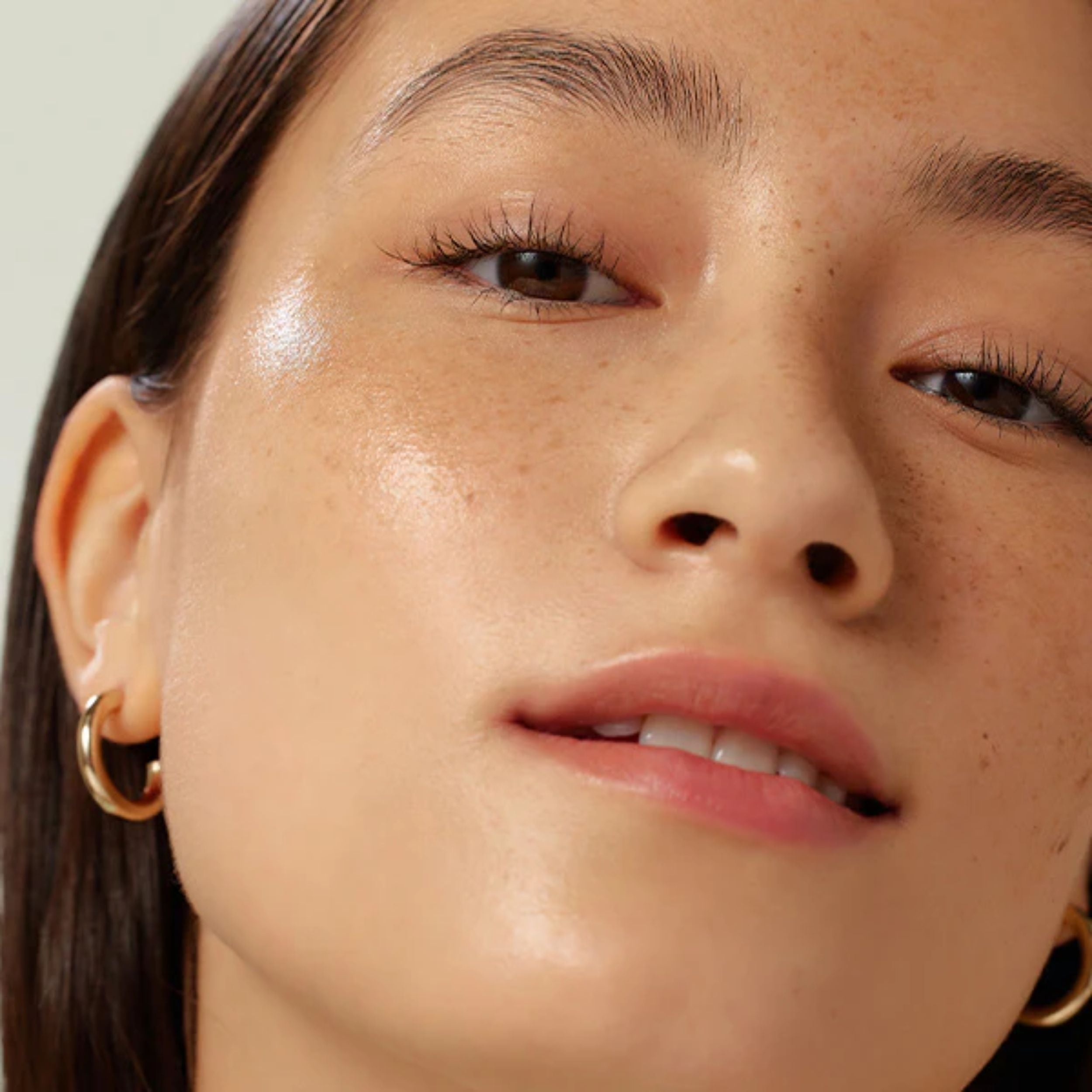 Close-up of a person wearing gold hoop earrings with a neutral background