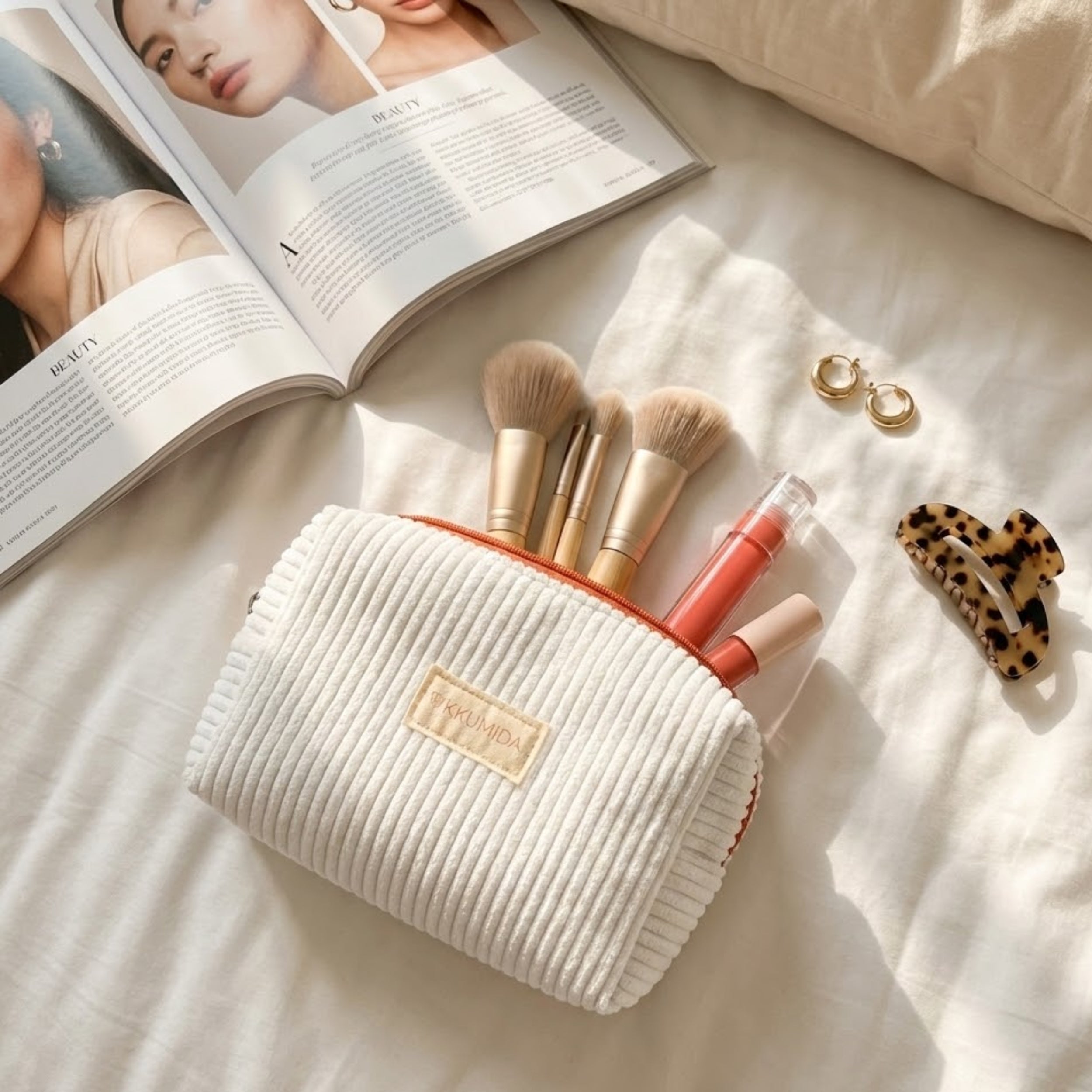 Makeup set with brushes, lip gloss, and earrings on a bed with an open magazine.