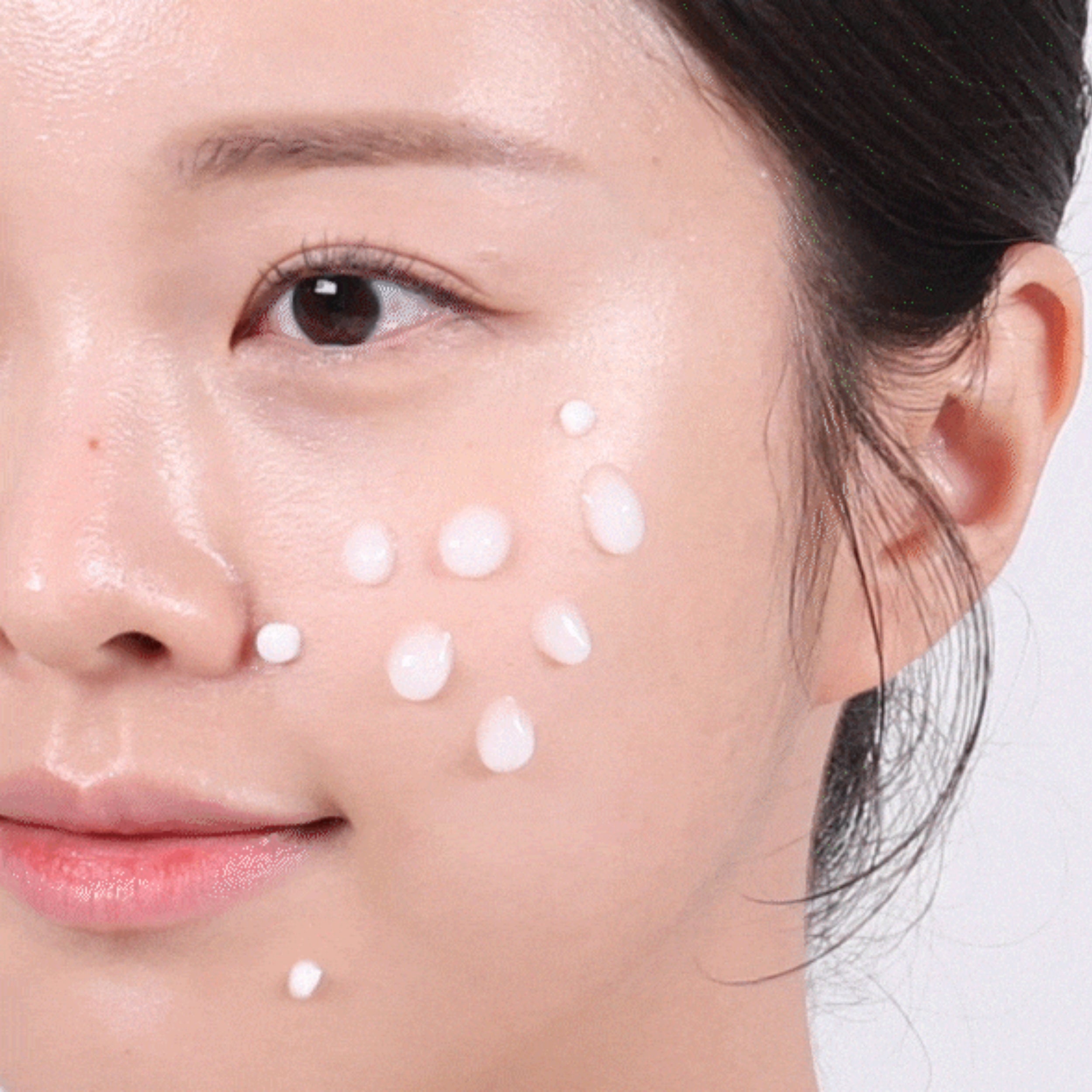 Close-up of a woman's face with white dots on her cheek, possibly showing skincare product application.