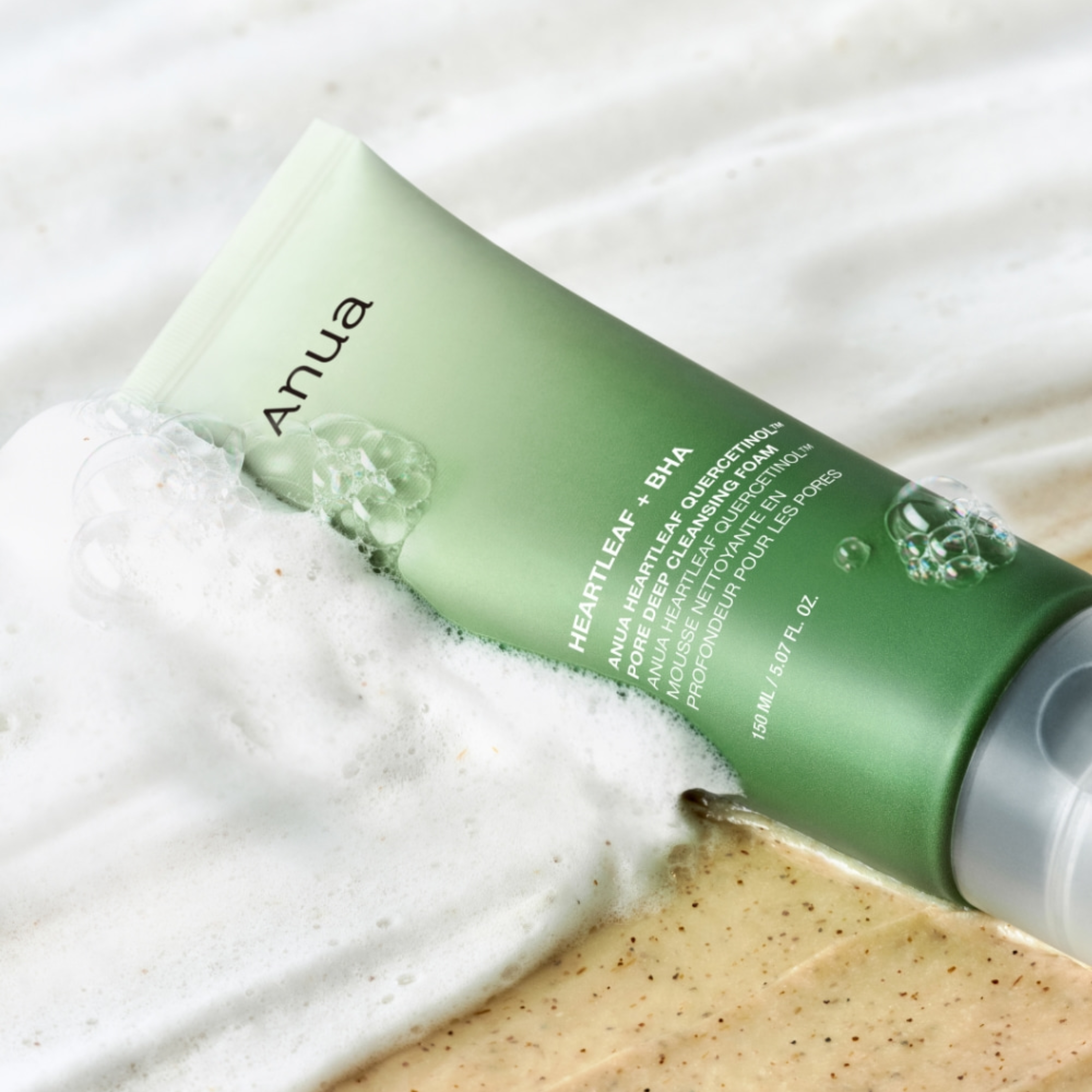 Green Anua facial cleanser tube with foam on a white towel