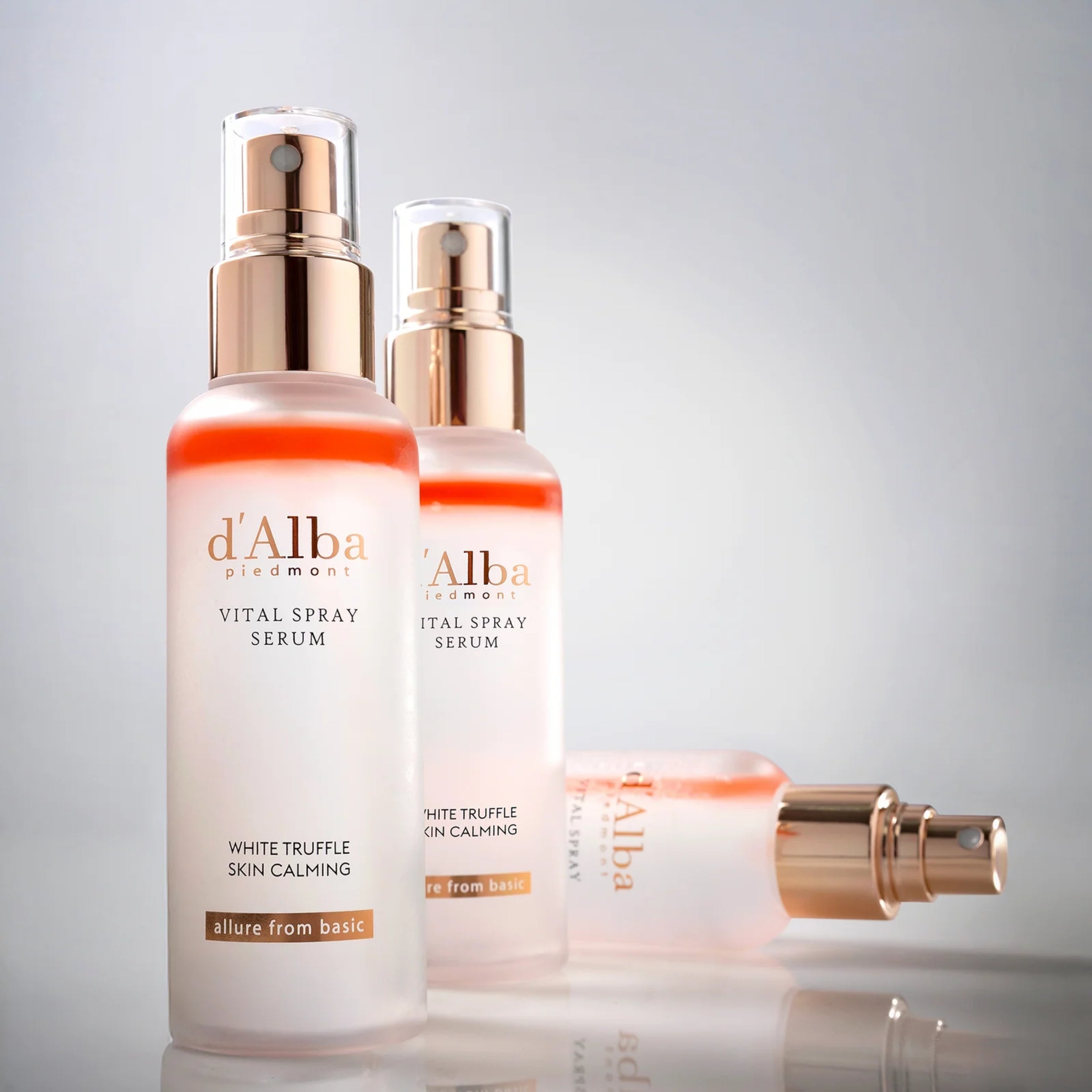 Two dAlba Vital Spray Serum bottles on a reflective surface with a gray background