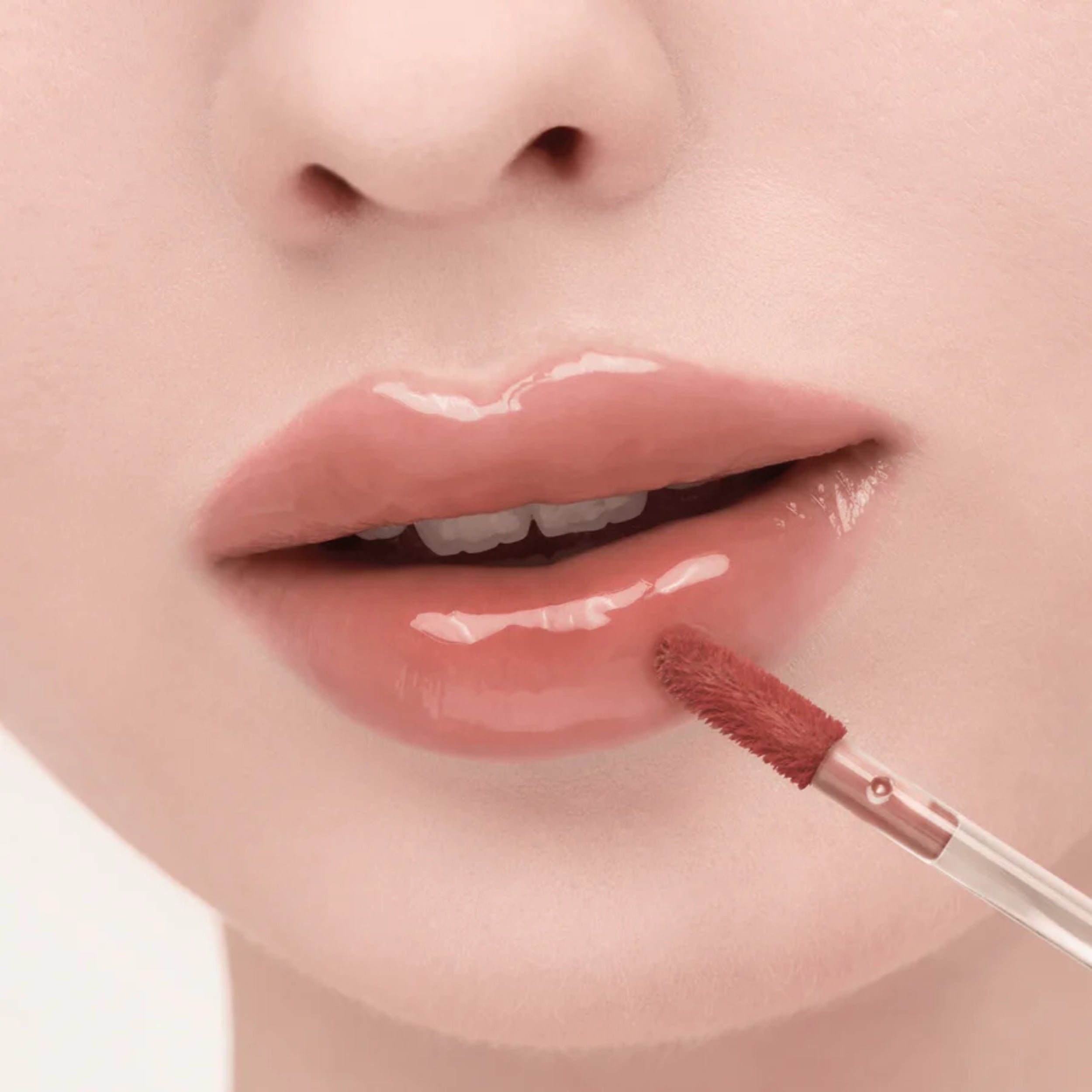 Close-up of a person applying lip gloss with a brush on a light background