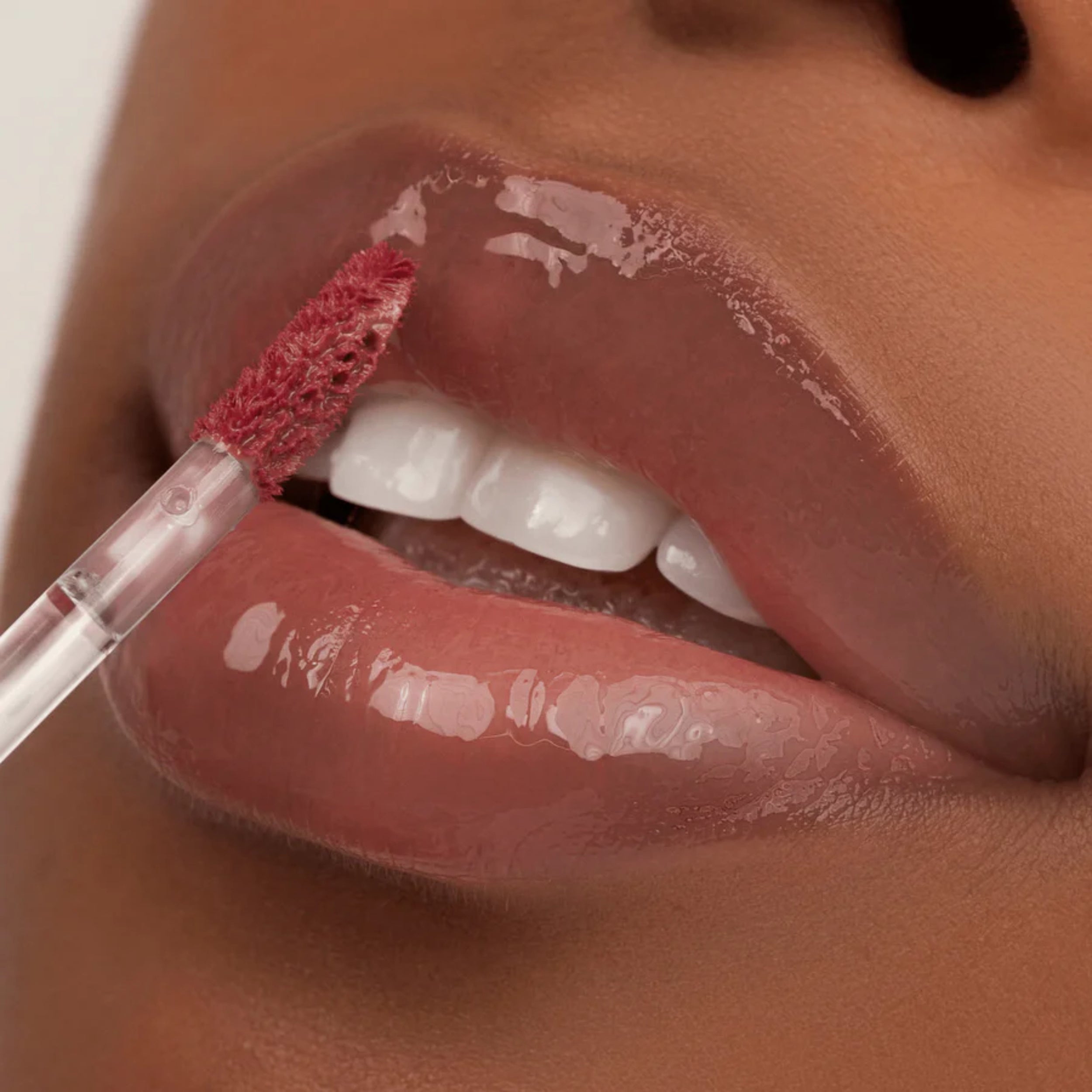 Close-up of a person applying pink lip gloss with a brush to their lips.